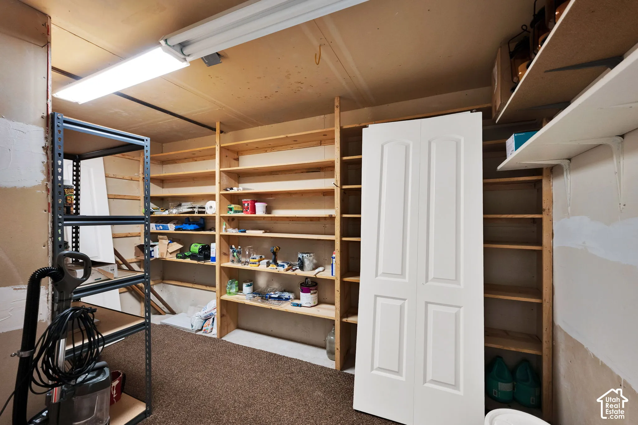 Storage room featuring wall-to-wall built-in wood shelving, overhead fluorescent lighting, and a bi-fold door