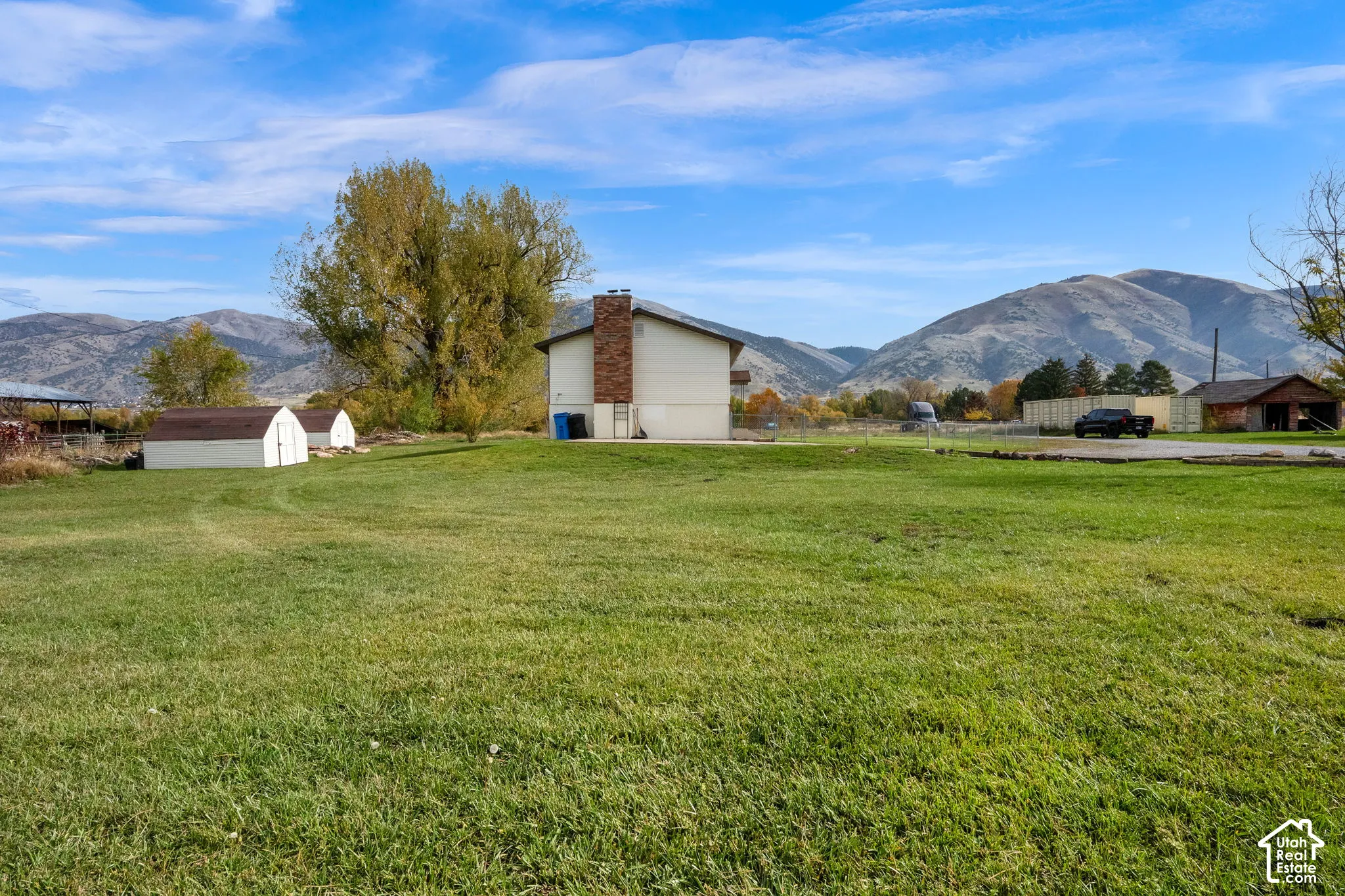 Expansive lot featuring a manicured lawn, external brick chimney, auxiliary storage structures, and mountain backdrop