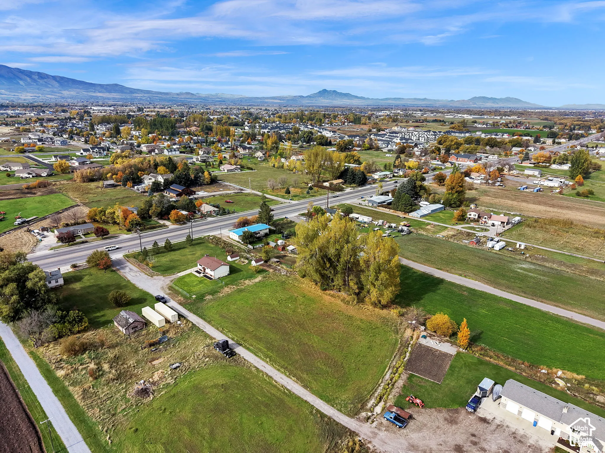 Aerial perspective of expansive open land featuring mature trees, a gravel access path, and mountain range backdrop