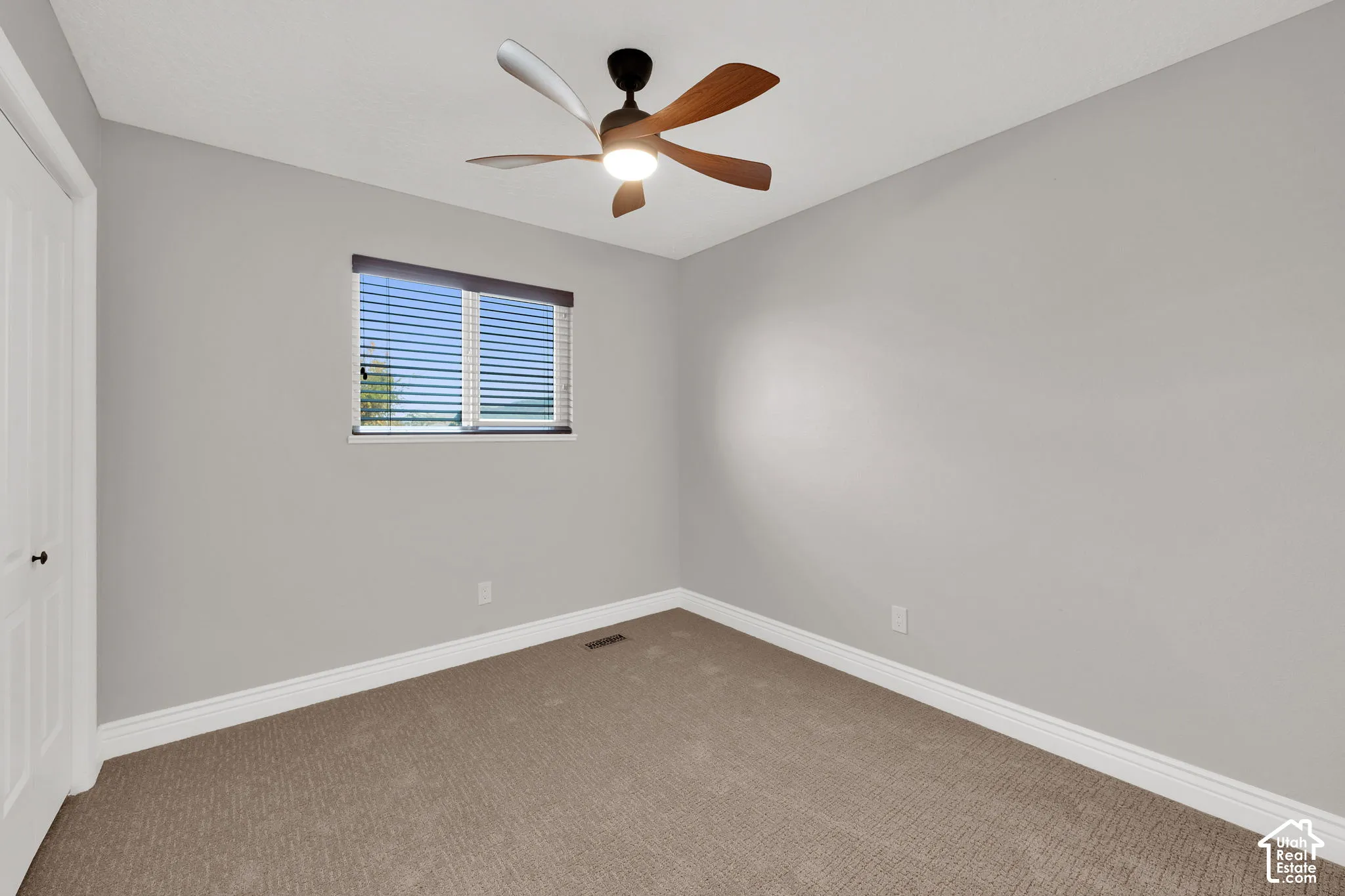 Neutral wall palette, ceiling fan with integrated lighting, carpeted flooring, and a single-panel window with horizontal blinds