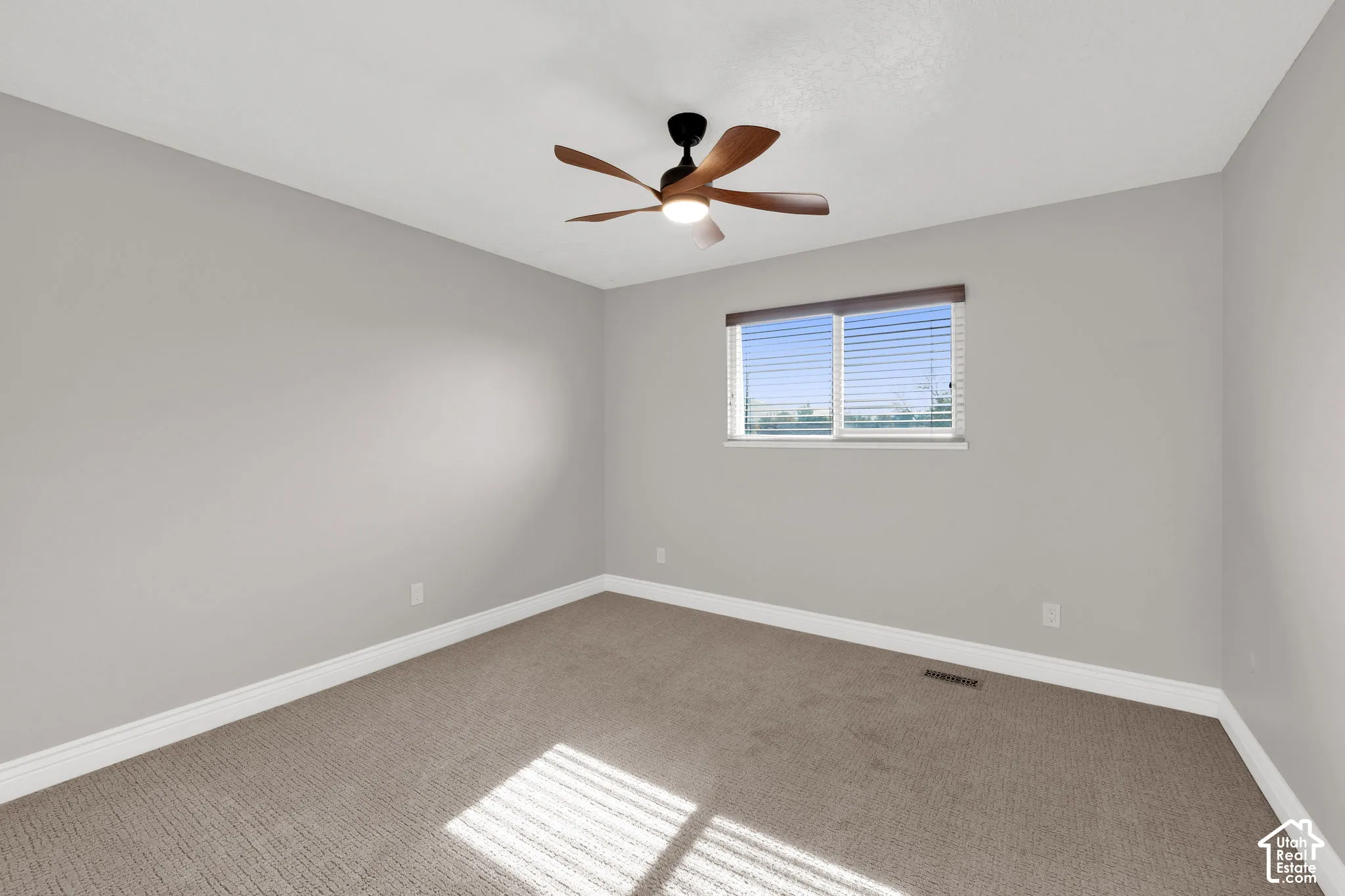 Neutral interior space featuring carpeted flooring, light grey walls, a ceiling fan with integrated lighting, and a single-pane window with horizontal blinds