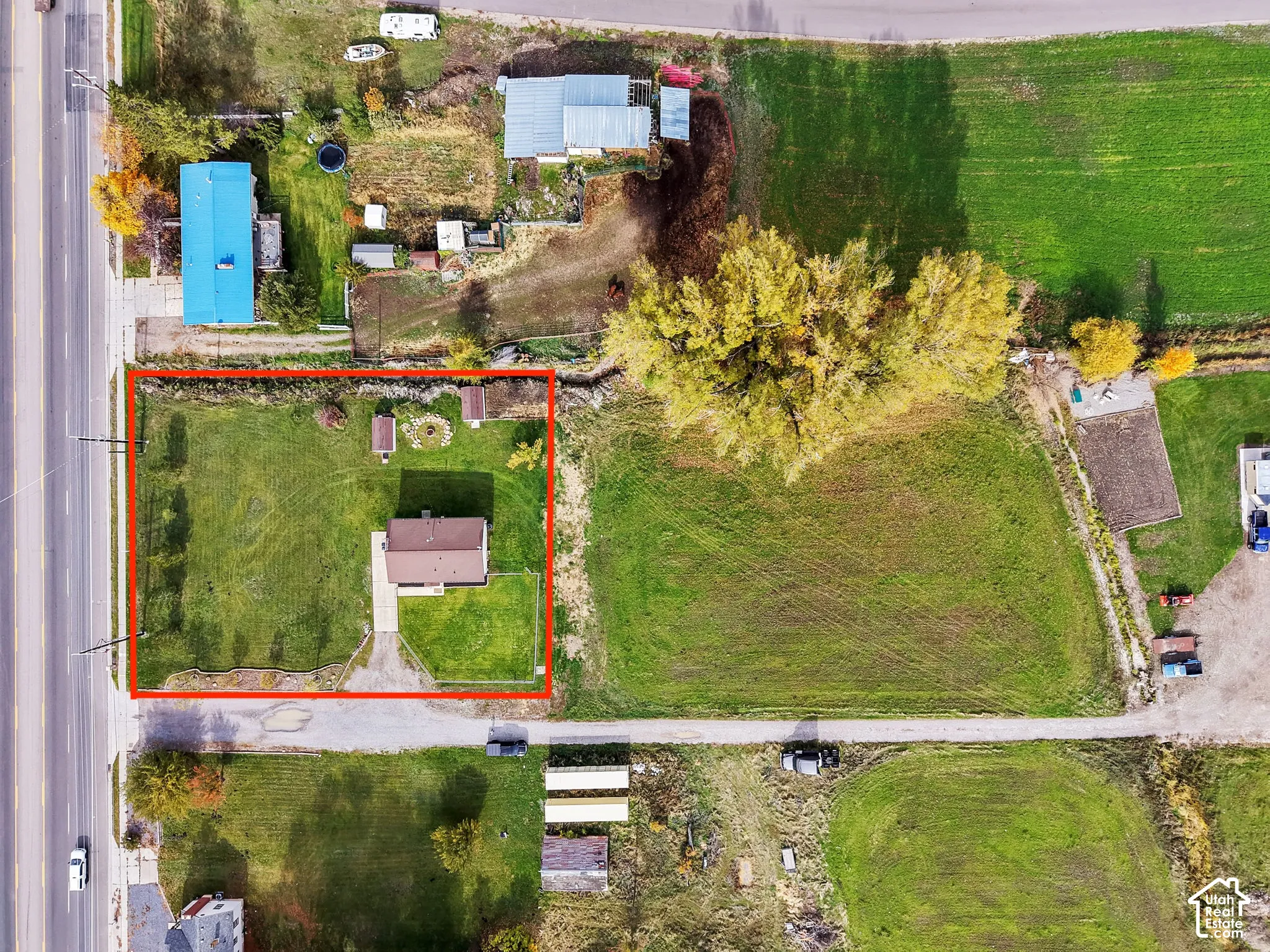 Aerial view of property featuring a residential structure, paved driveway, detached storage shed, and expansive grass-covered grounds