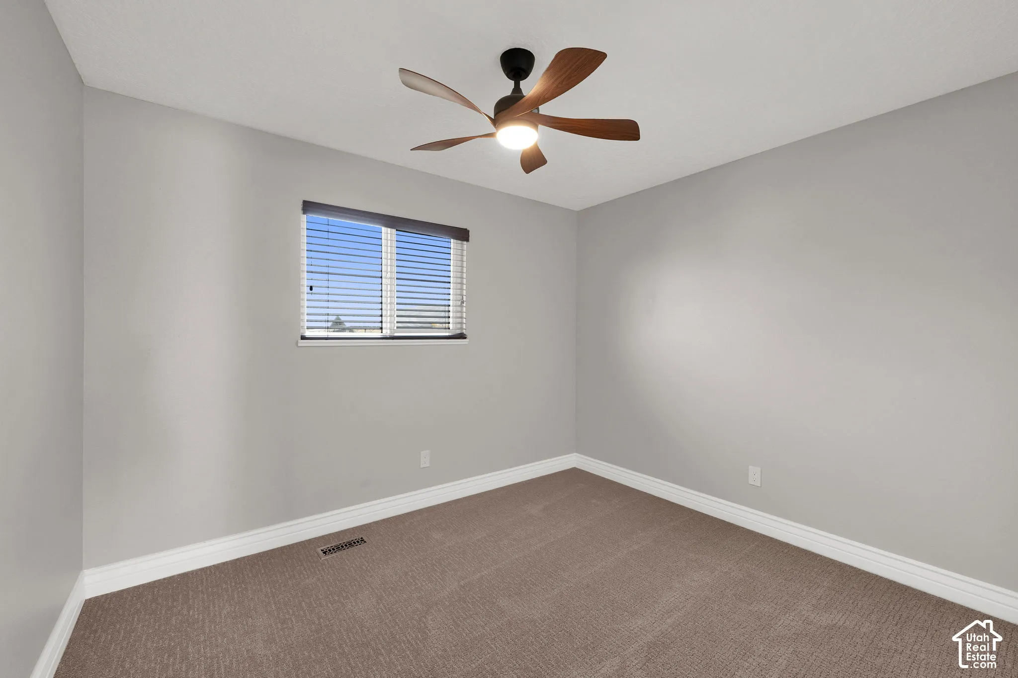 Neutral-toned interior space featuring wall-to-wall carpeting, a multi-blade ceiling fan with integrated lighting, and a window fitted with horizontal blinds