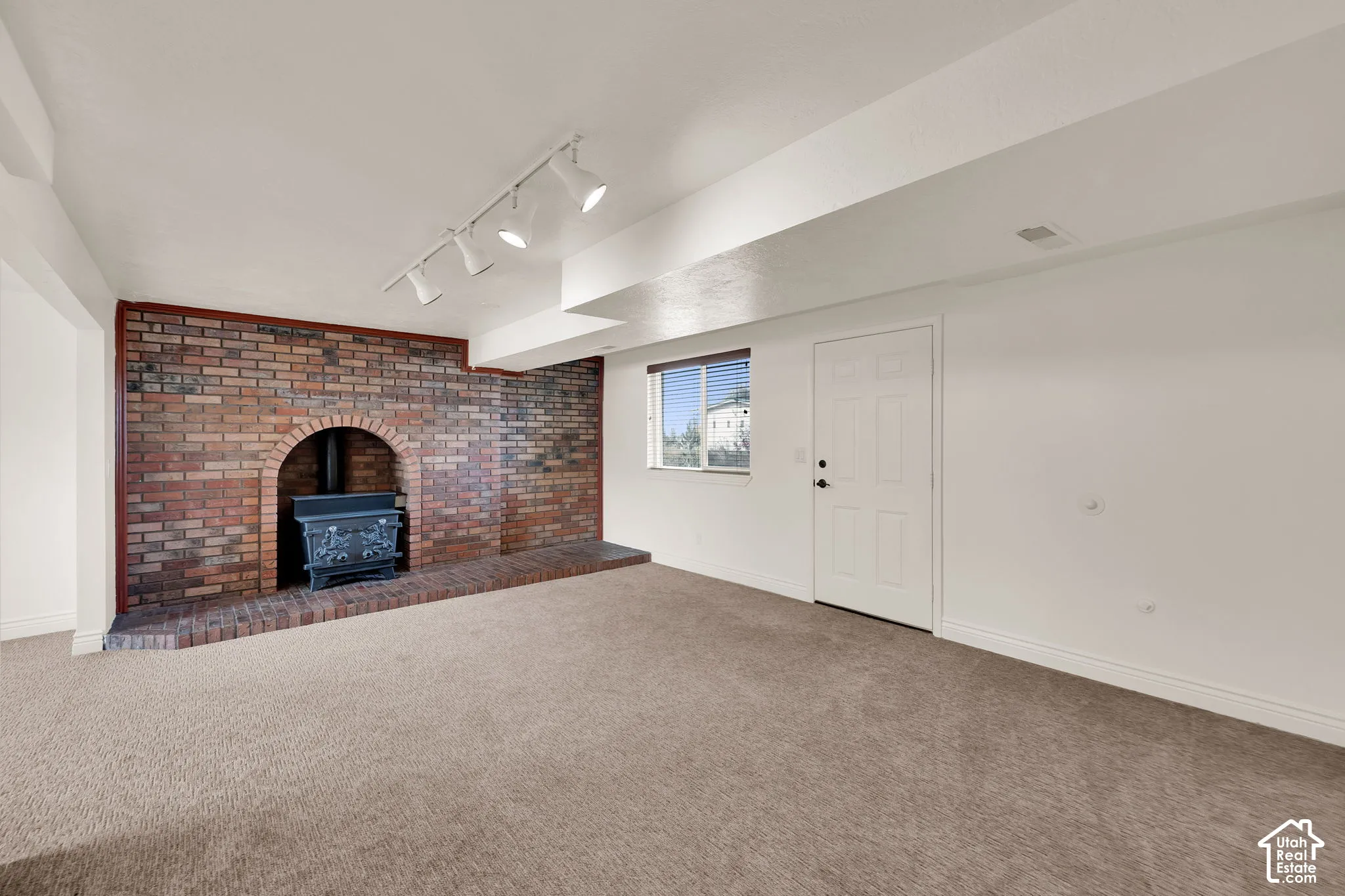 Interior space featuring a brick accent wall with an arched hearth, a cast-iron stove, neutral carpeting, and adjustable track lighting