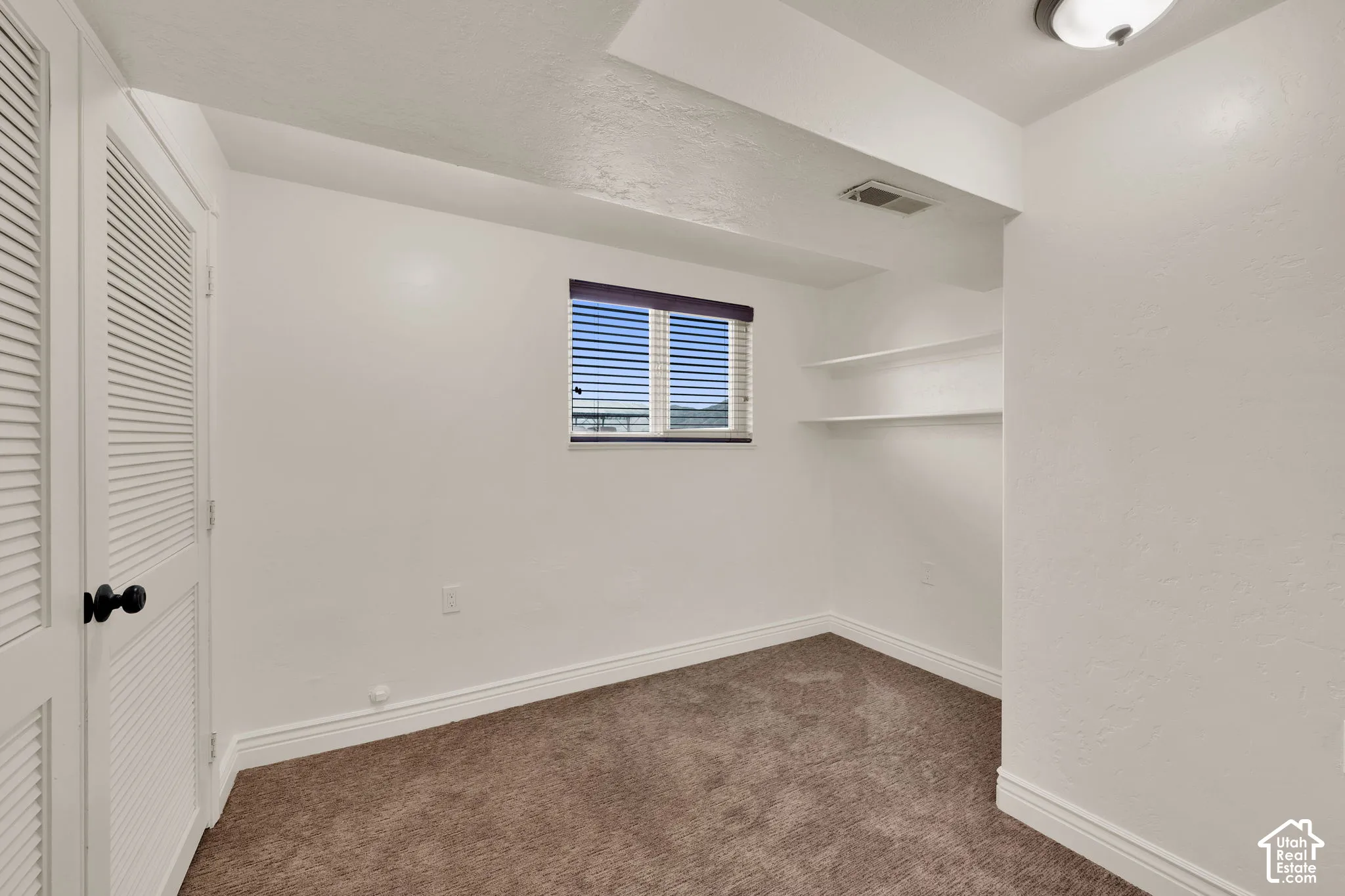 Neutral-toned carpeting, louvered closet doors with matte black hardware, recessed wall shelving, and a dual-pane window