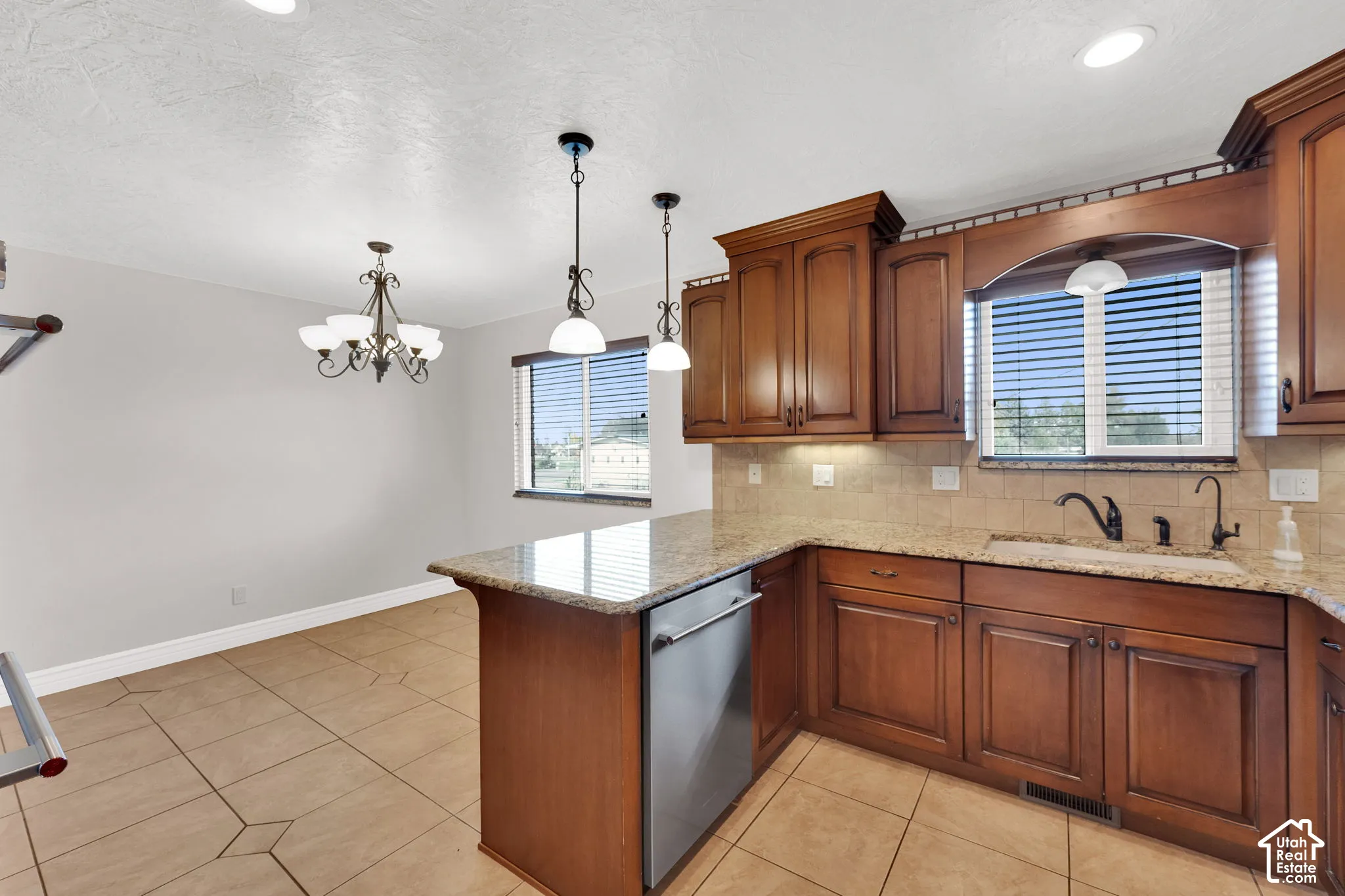 Kitchen featuring stained wood cabinetry, stone countertops, stainless steel dishwasher, tile backsplash, and ceramic tile flooring with decorative inserts