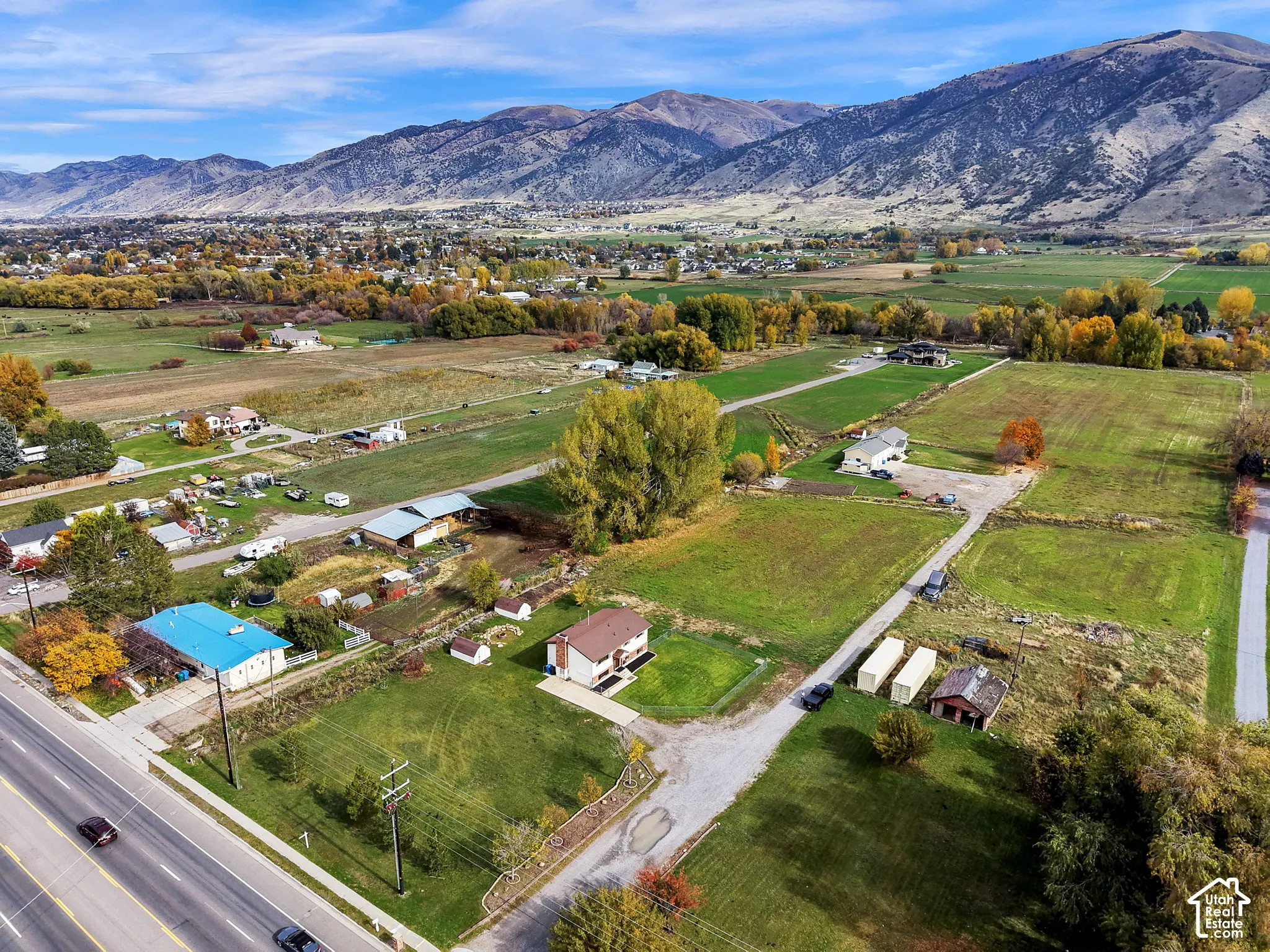 Aerial perspective of a multi-acre property featuring expansive open grounds, a gravel driveway, mature trees, and a mountain backdrop