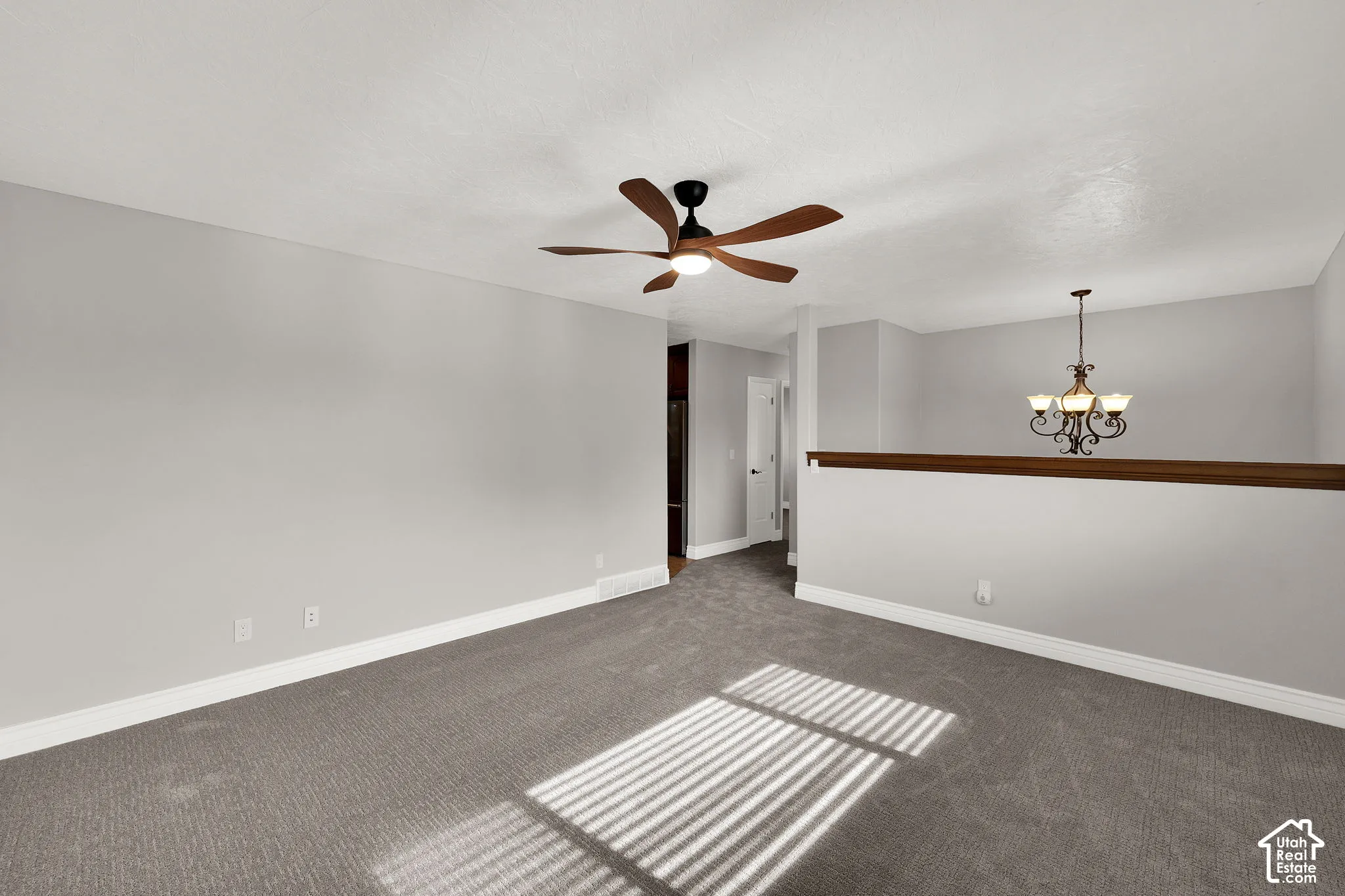 Neutral-toned interior space featuring wall-to-wall carpeting, a five-blade ceiling fan with integrated lighting, and a multi-arm chandelier with glass shades, finished with a wood-capped pony wall