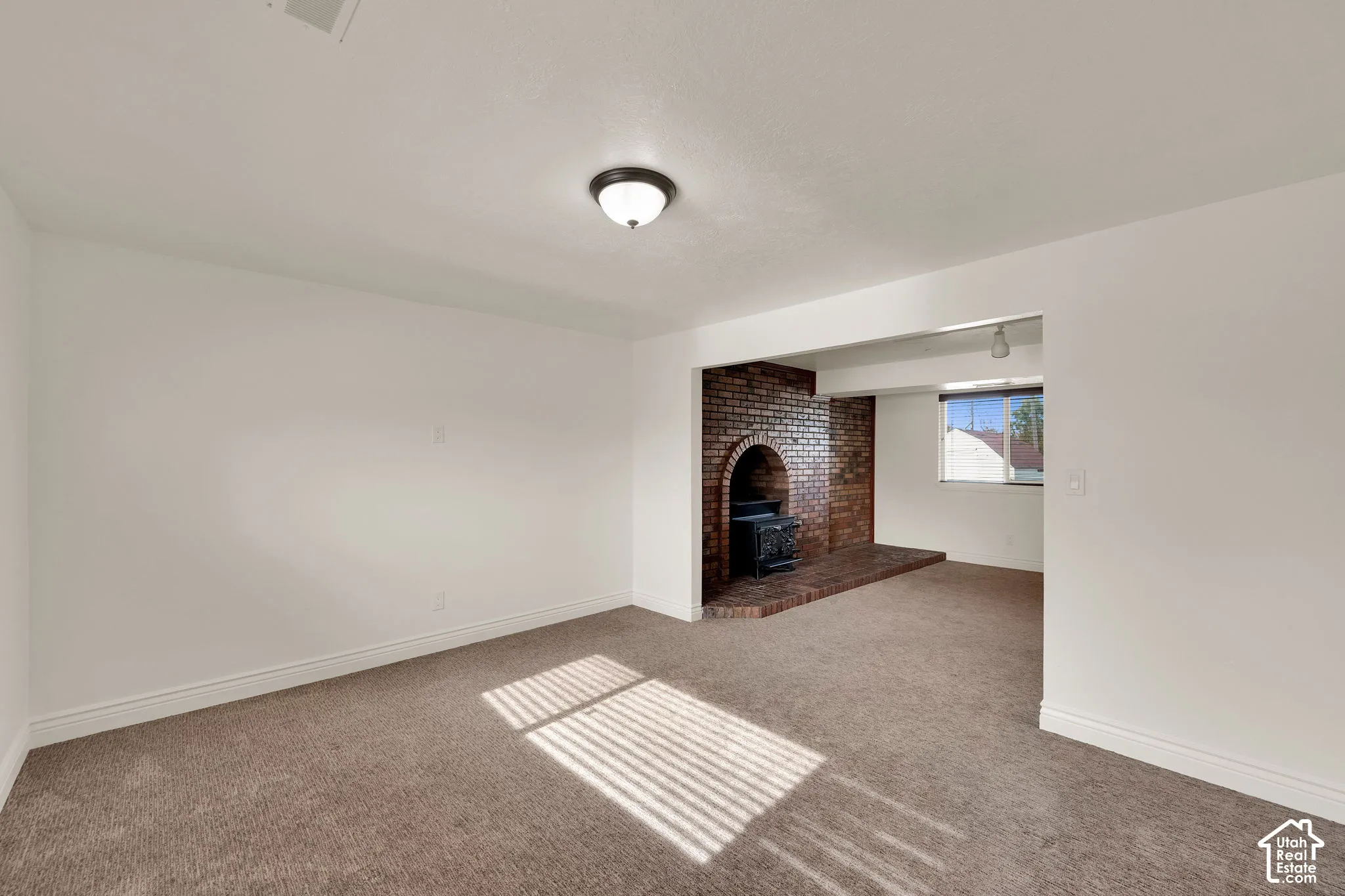 Interior space featuring neutral wall tones, carpeted flooring, and a recessed brick fireplace with an arched hearth and cast-iron stove