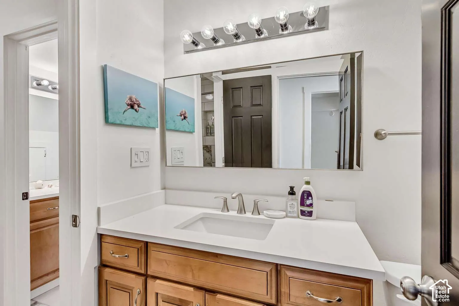 Bathroom vanity featuring a white composite countertop, an integrated rectangular sink, wood-finish cabinetry, a large frameless mirror, and a six-light vanity fixture