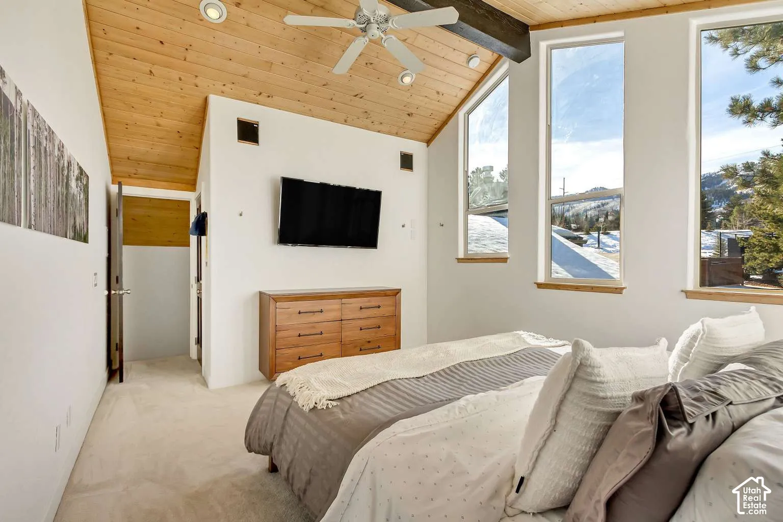Vaulted wood-plank ceiling featuring exposed structural beams, ceiling fan with integrated lighting, and oversized vertical windows