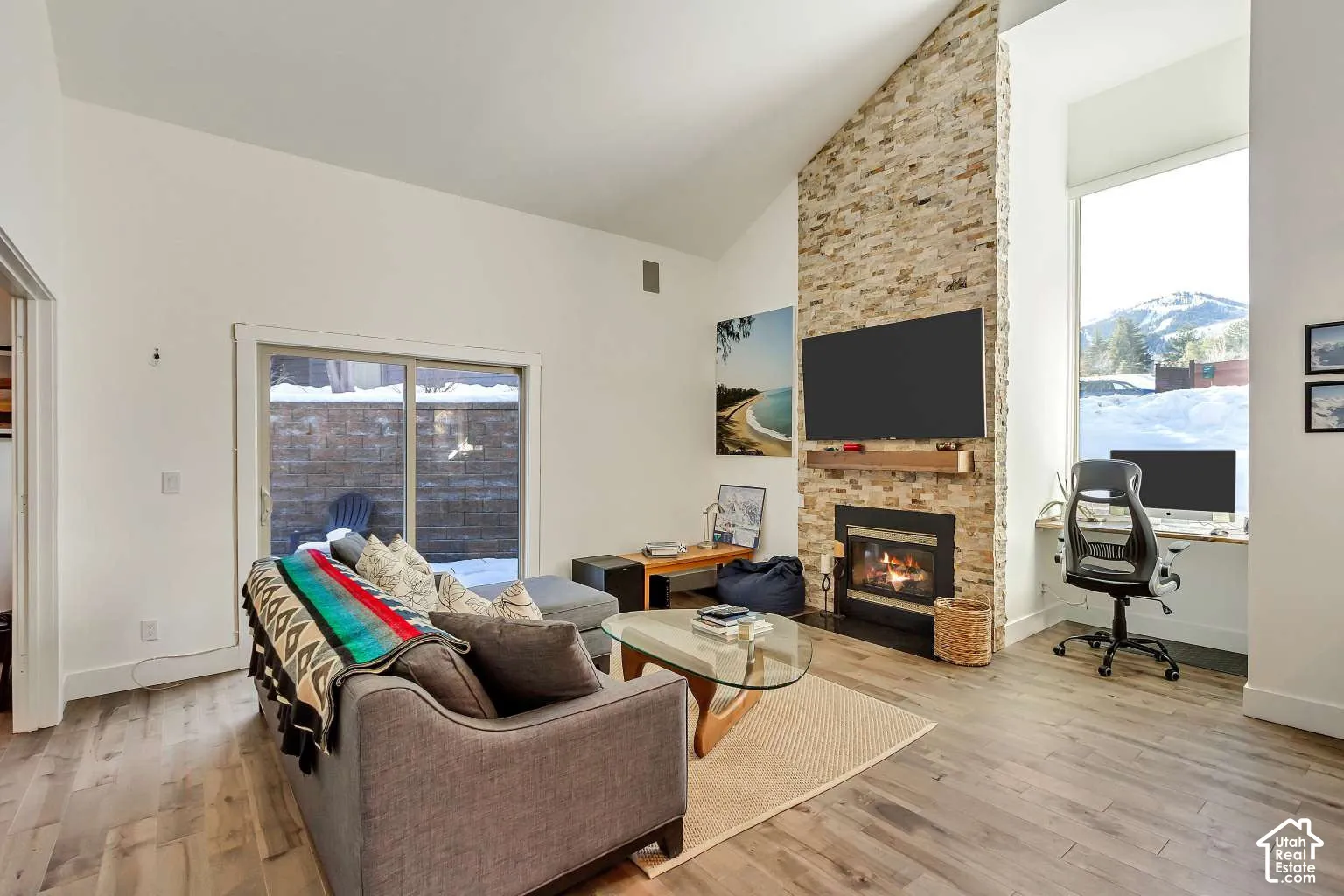 Vaulted ceiling, floor-to-ceiling stone-veneer fireplace, wood-finish flooring, sliding glass door, and large window with mountain backdrop