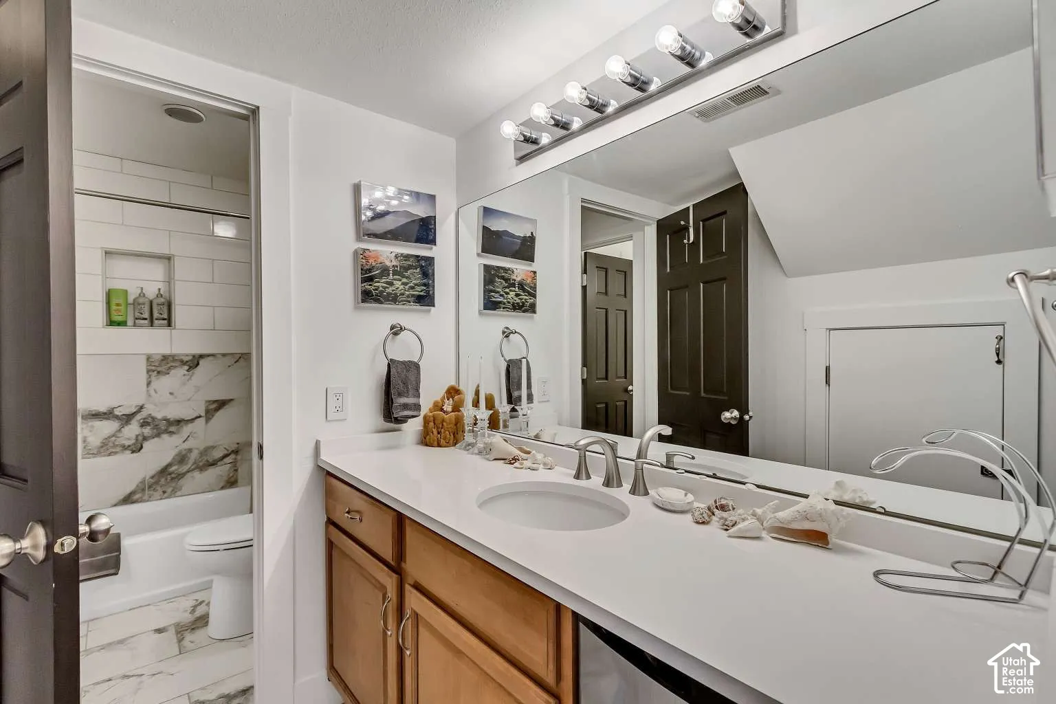 Bathroom featuring wood cabinetry, a wide countertop with a recessed basin, a full-width wall mirror, and a tile-surround shower with a built-in recessed niche