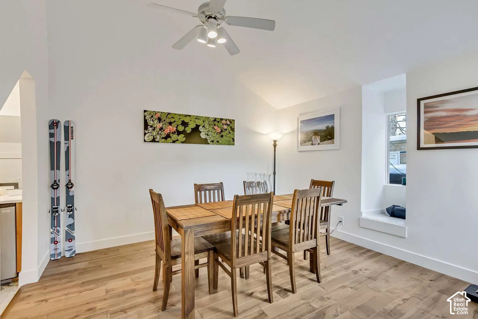 Vaulted ceiling featuring a central light fixture with an integrated ceiling fan, wood-finish flooring, and a built-in window seat