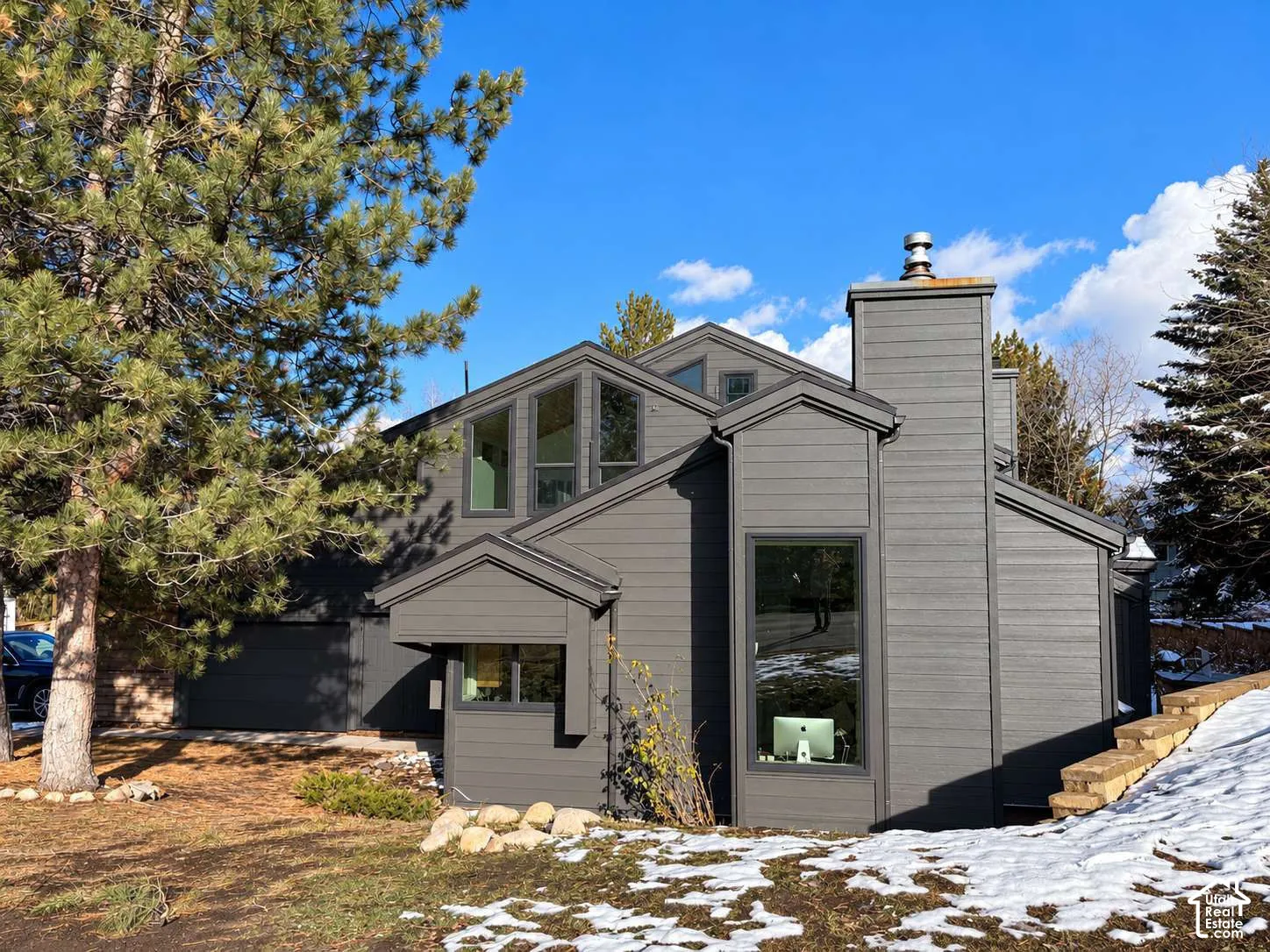 Multi-level exterior featuring dark horizontal siding, prominent chimney stack, oversized geometric windows, and a built-in multi-car garage