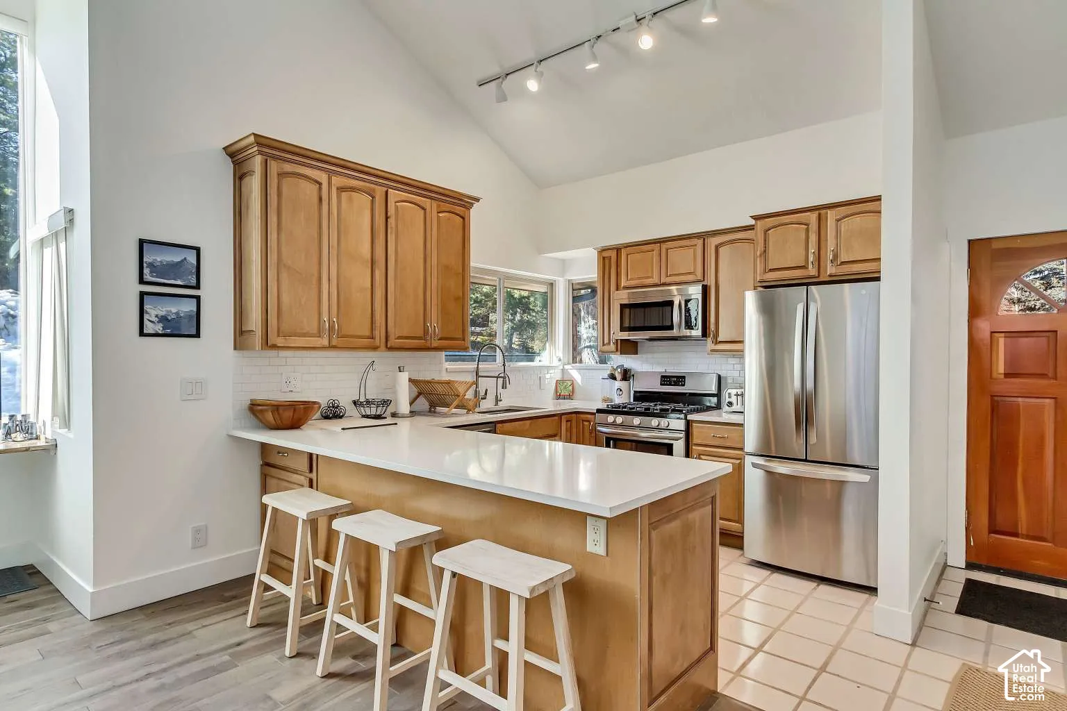 Kitchen featuring vaulted ceilings, light-tone wood cabinetry, white stone countertops, stainless steel appliances, and tile flooring