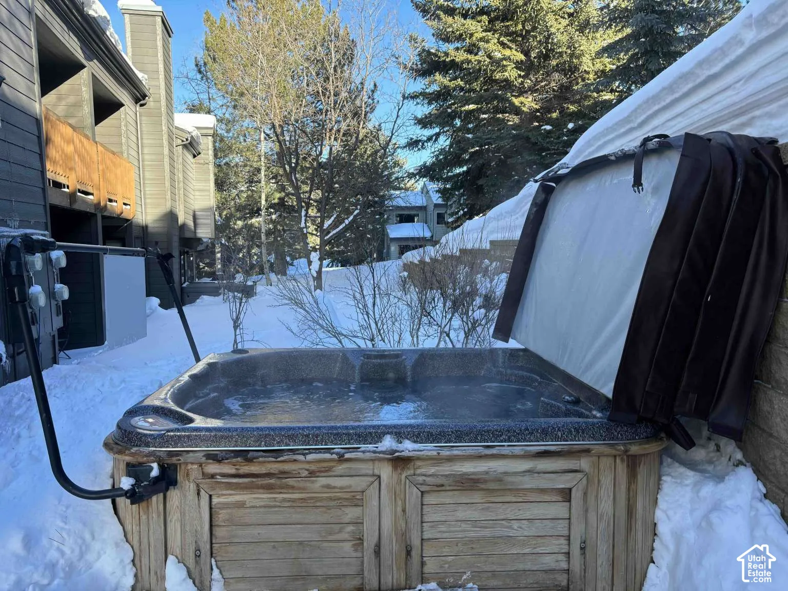 Outdoor hot tub featuring wood-finish cabinetry, a mechanical cover lift, and a textured acrylic interior