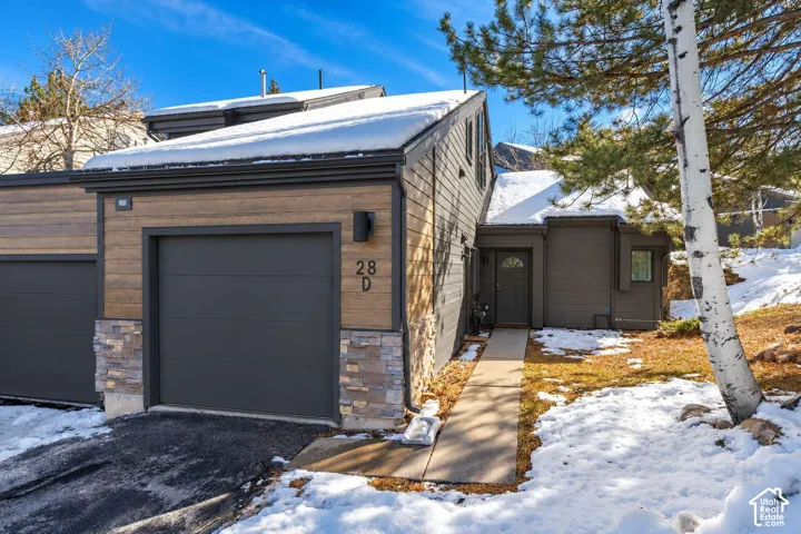 Exterior featuring horizontal wood-tone siding, stone veneer accents, multi-level rooflines, and an attached garage