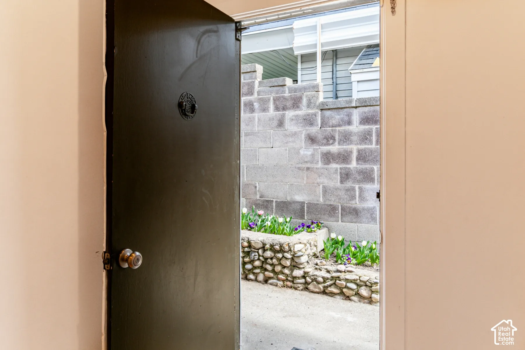 Solid core door with circular metal knocker and metallic knob, concrete block perimeter wall, stone-accented raised garden bed, and integrated landscaping