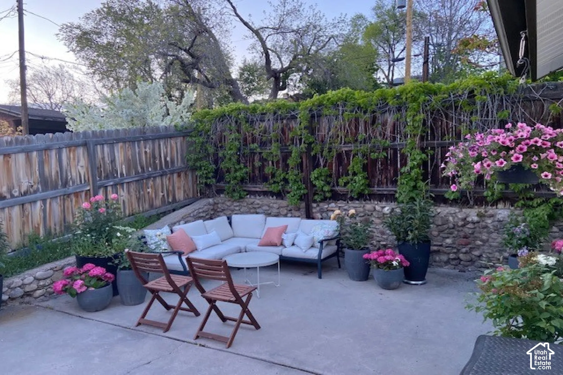 Concrete patio featuring a natural stone retaining wall, wooden perimeter fencing, and mature climbing vegetation