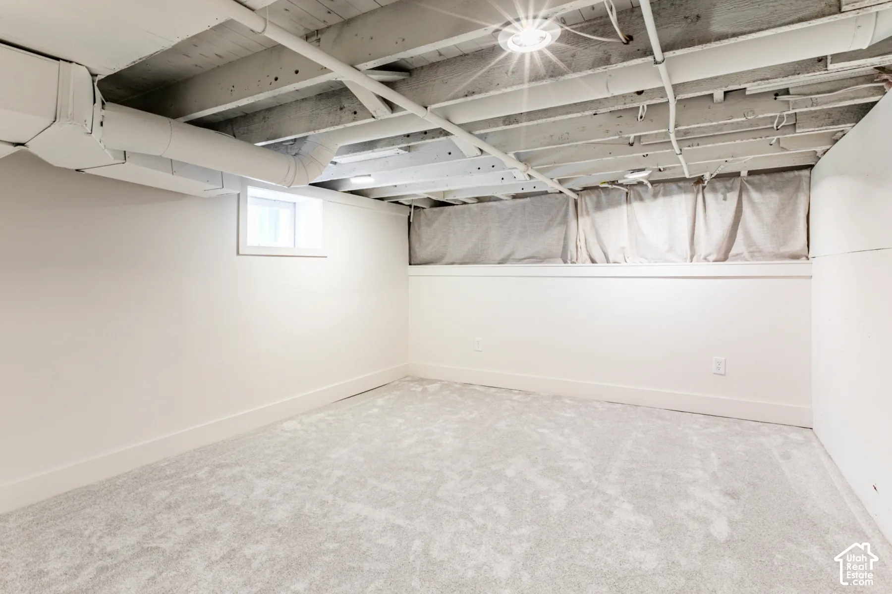 Finished room with neutral carpeting, painted white walls, recessed ceiling lighting, and exposed painted joists