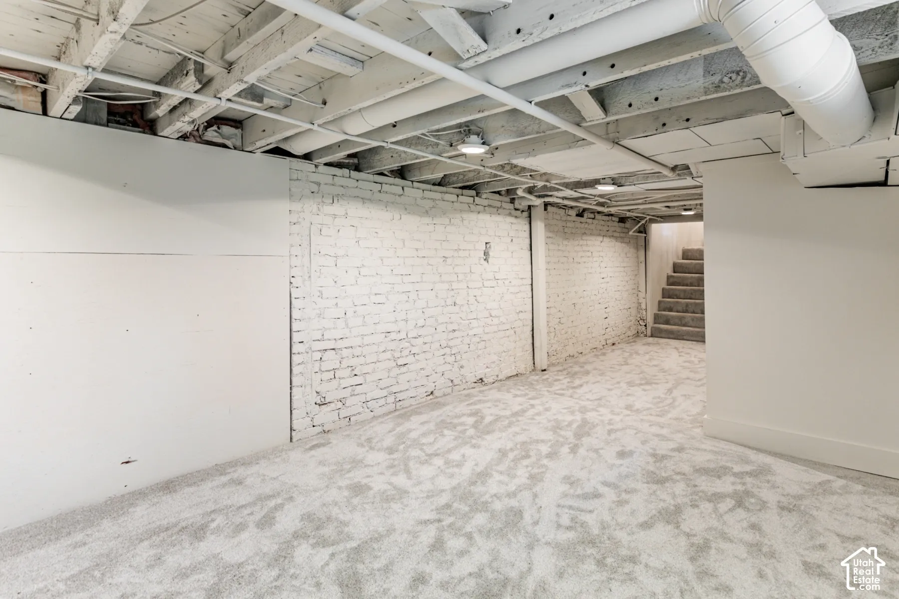 Unfinished space featuring white-painted exposed brick walls, wall-to-wall carpeting, and an exposed joist ceiling with integrated lighting