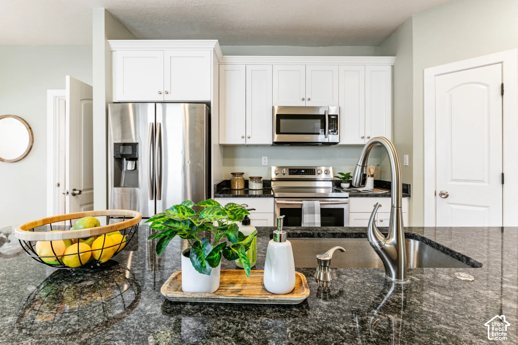 Kitchen featuring white shaker-style cabinetry, stone countertops, stainless steel appliances, and a polished chrome high-arc kitchen faucet with integrated sprayer