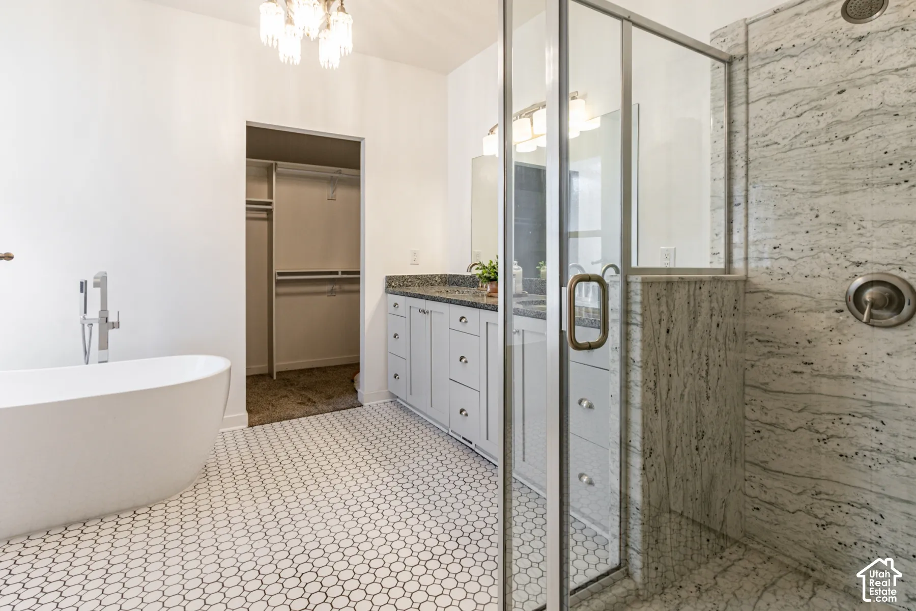 Freestanding soaking tub, stone-surround walk-in shower with glass enclosure, dual-sink vanity with stone countertop, hexagon tile flooring, and built-in closet shelving