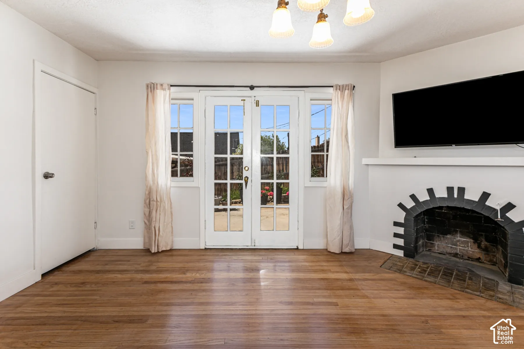 Room featuring wood-finish flooring, a fireplace with a decorative stone arch, dual French doors with glass panes, and a multi-light chandelier