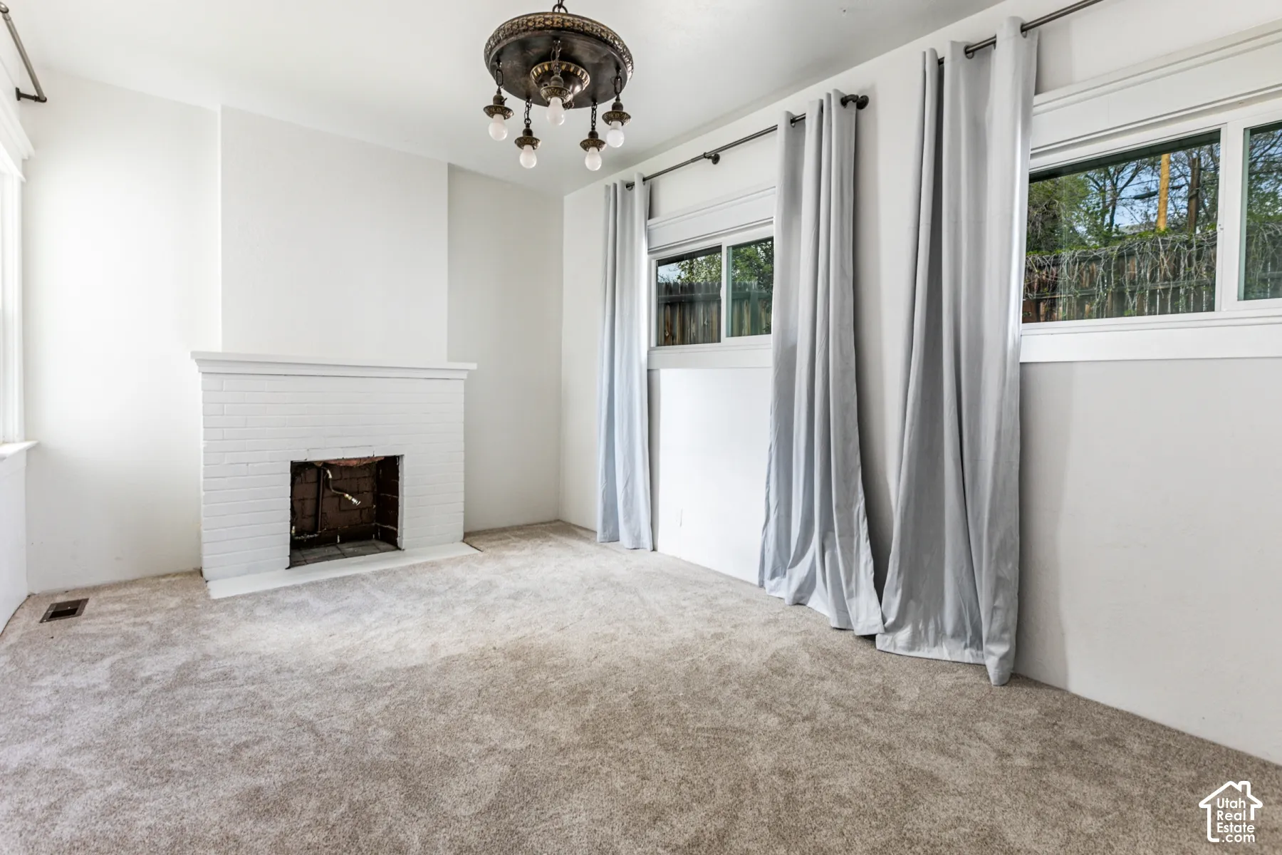 Painted brick fireplace, decorative multi-arm ceiling fixture, wall-to-wall carpeting, and sliding windows