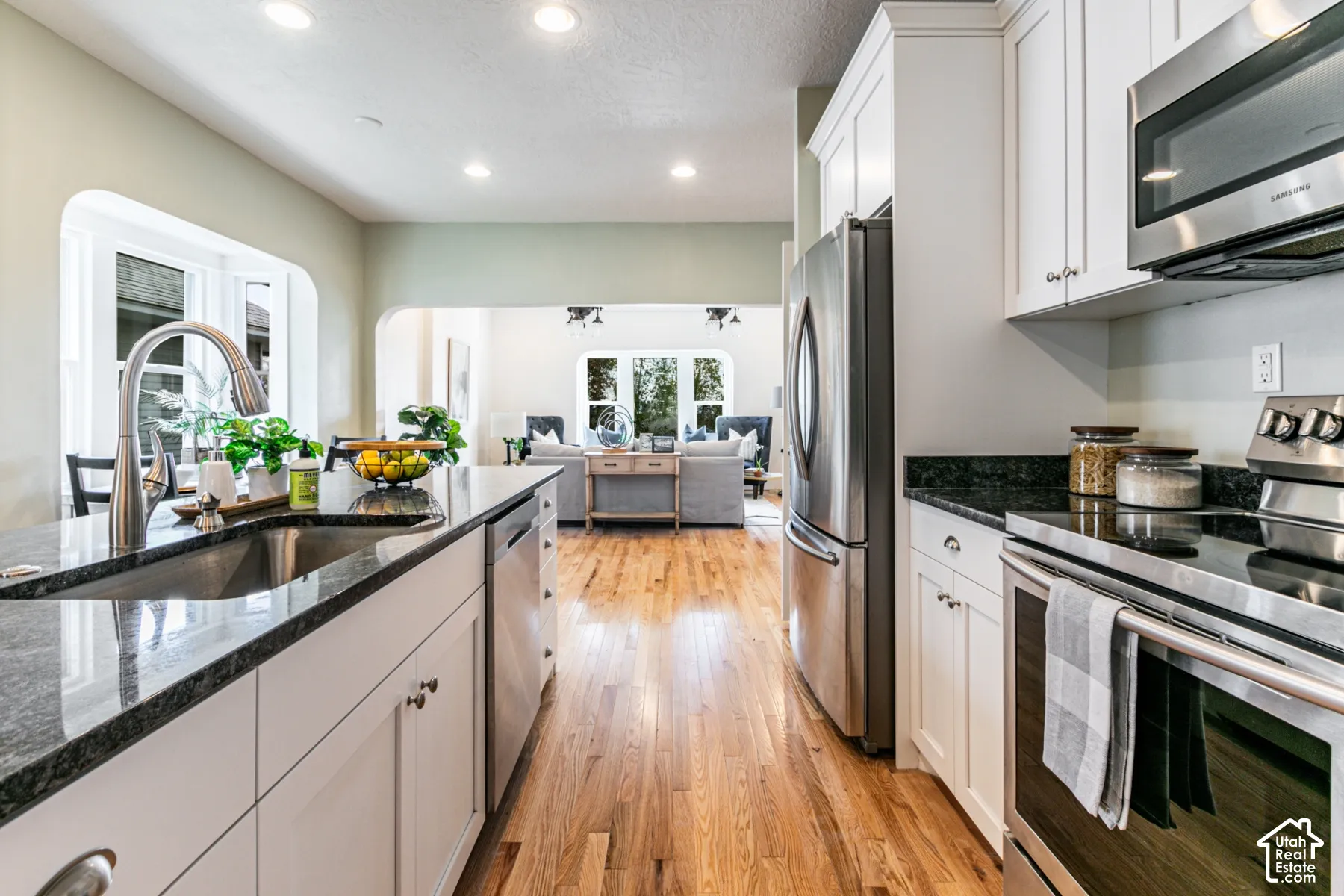 Kitchen featuring white cabinetry, stone countertops, stainless steel appliances, and wood-finish flooring