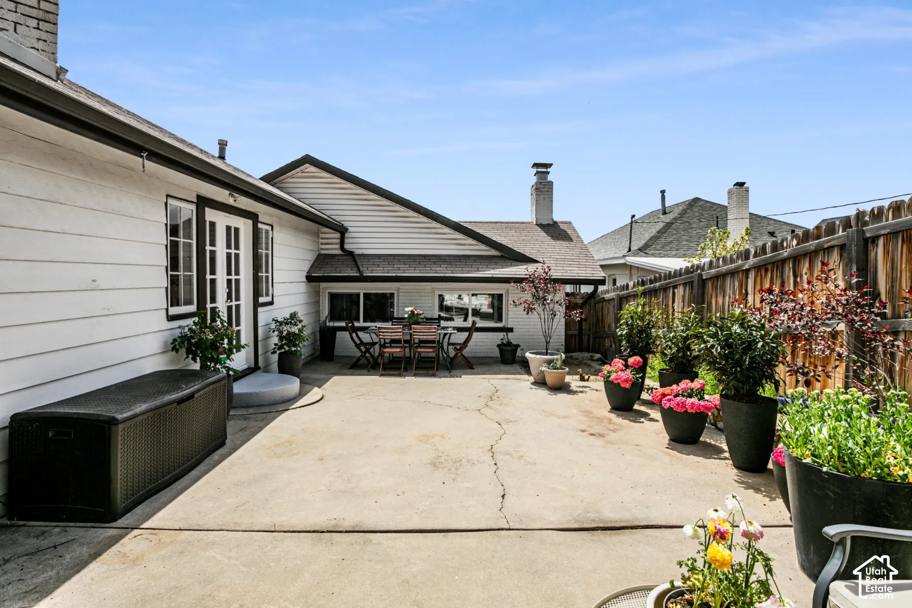 Concrete patio area featuring horizontal siding, double glass-paneled exterior doors, a wood fence perimeter, and brick chimney structures