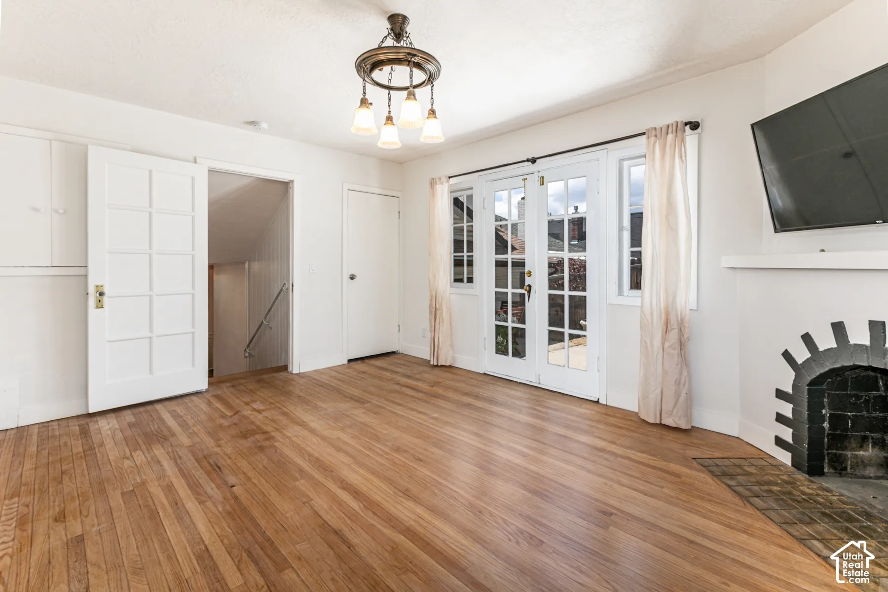 Interior space featuring wood-finish flooring, a traditional masonry fireplace with decorative tile surround, glass-paneled double doors, and a multi-light chandelier