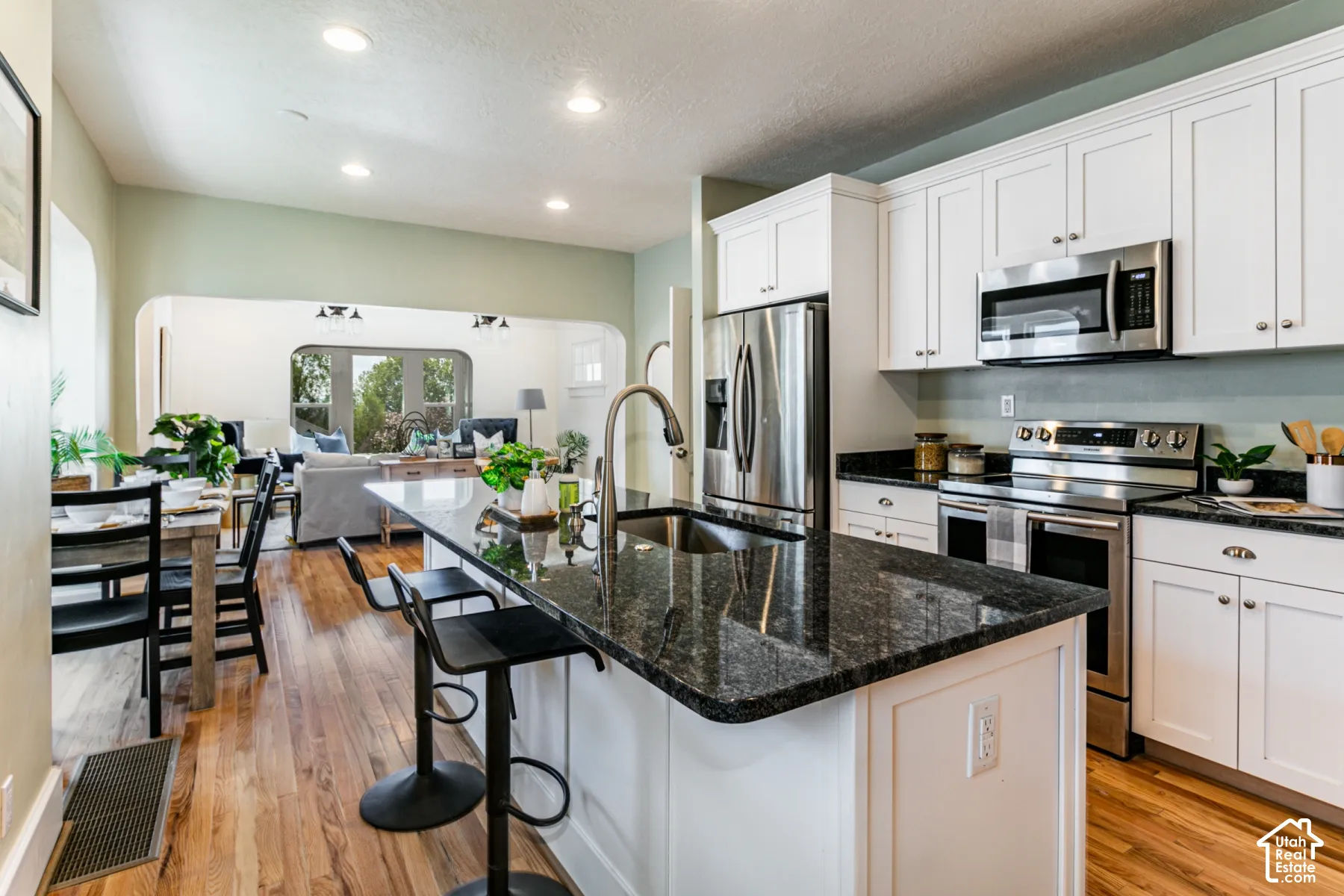 Kitchen featuring white cabinetry, an island with stone-finish countertops, stainless steel appliances, and wood-finish flooring