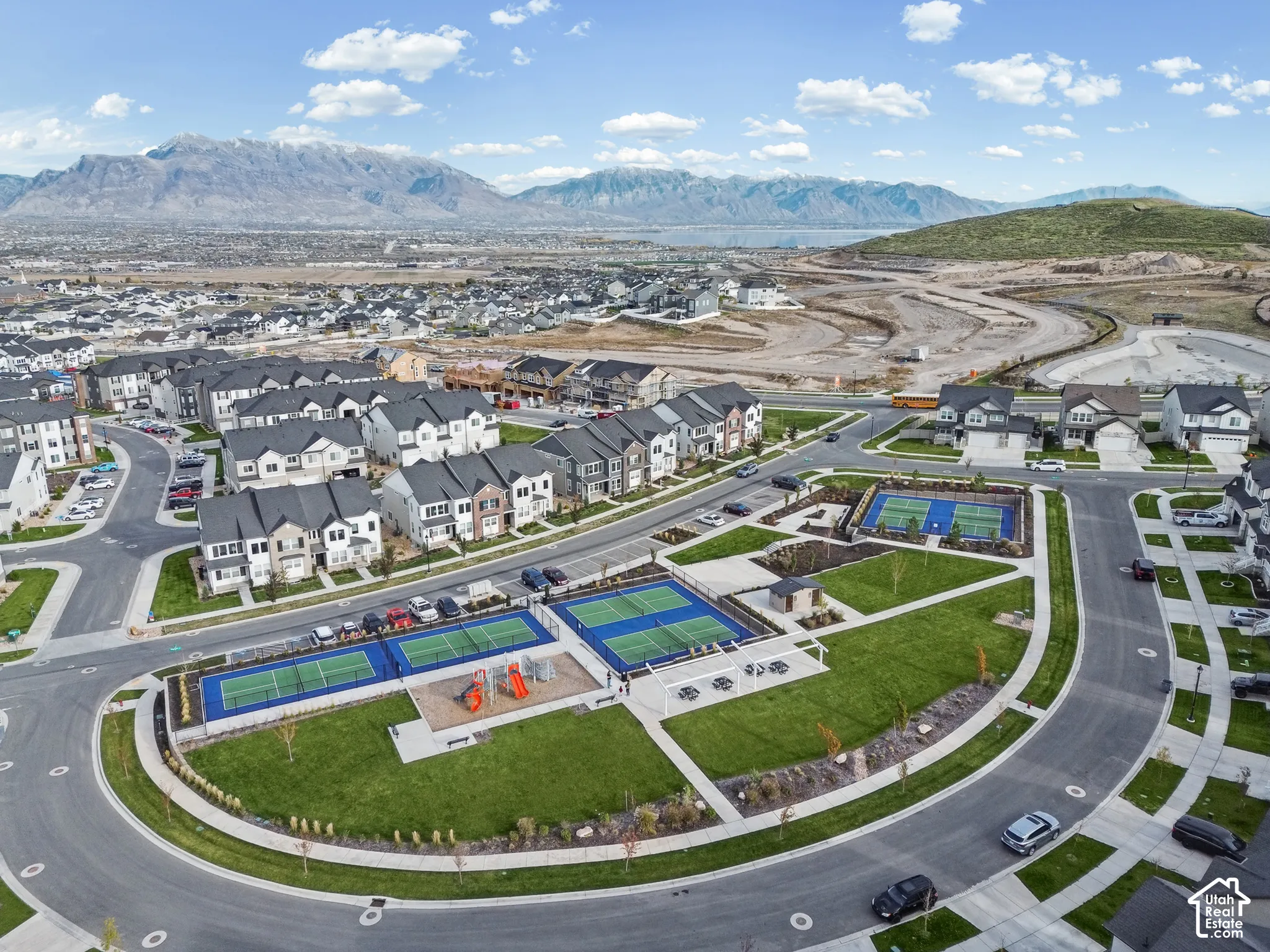 Community park featuring multi-use sports courts, playground equipment, manicured lawn areas, and mountain scenery