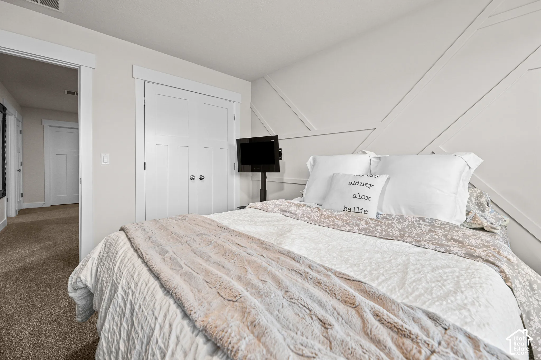 Bedroom featuring a geometric paneled accent wall, double-door closet with shaker-style detailing, and neutral-toned carpeting