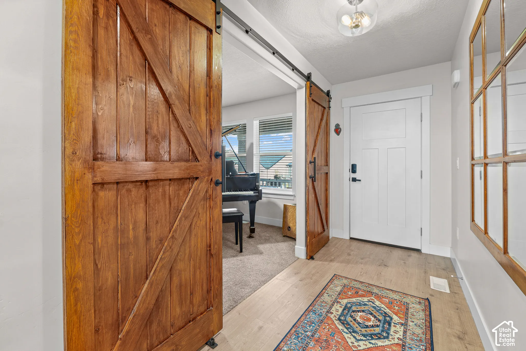 Stained wood barn-style sliding doors on matte black hardware, wood-finish flooring, white paneled entry door, and multi-pane grid wall mirror