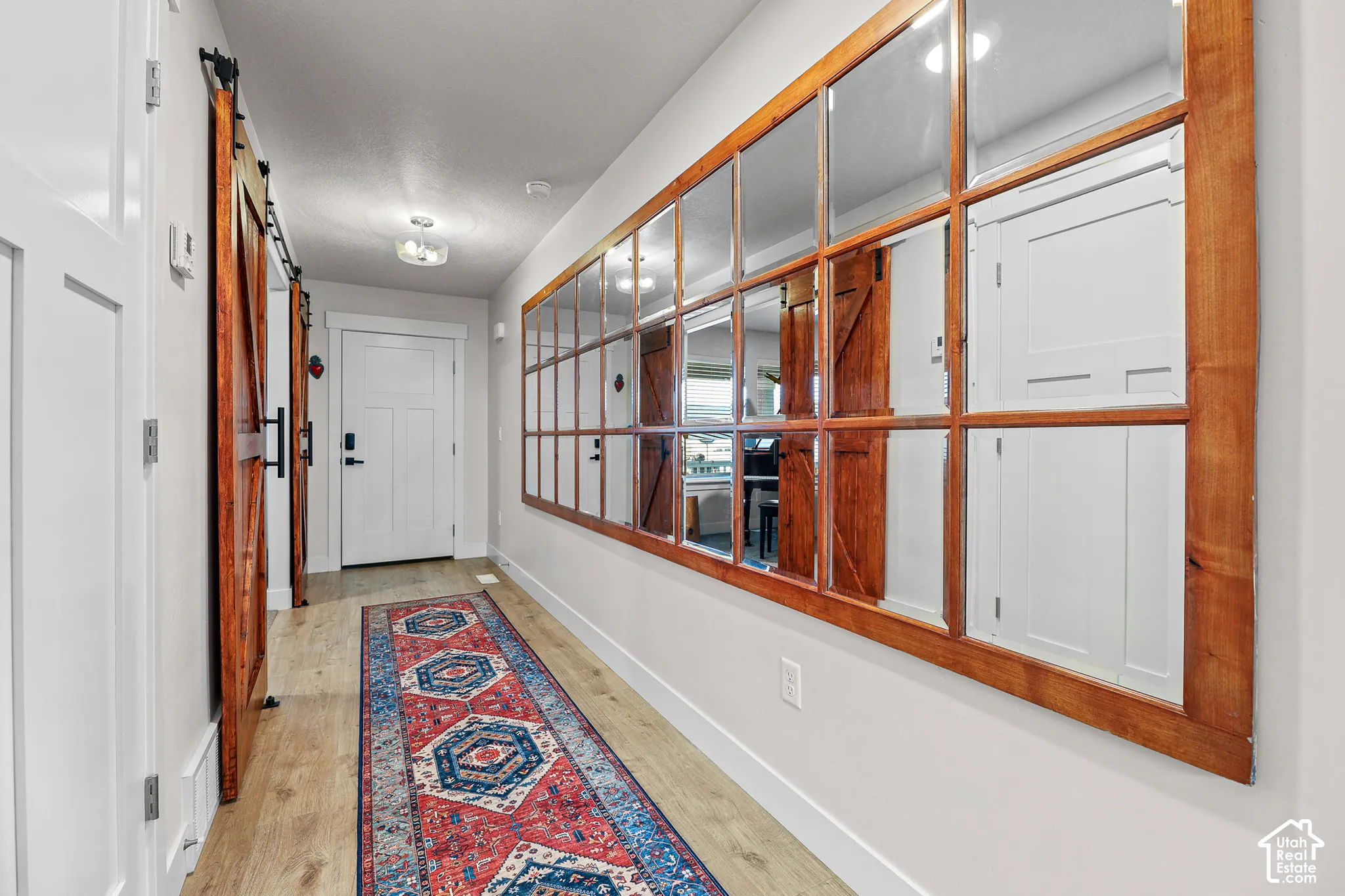 Hallway featuring wood-finish flooring, a wall-mounted multi-pane mirror with a wood frame, a sliding wood barn door, and a white paneled entry door