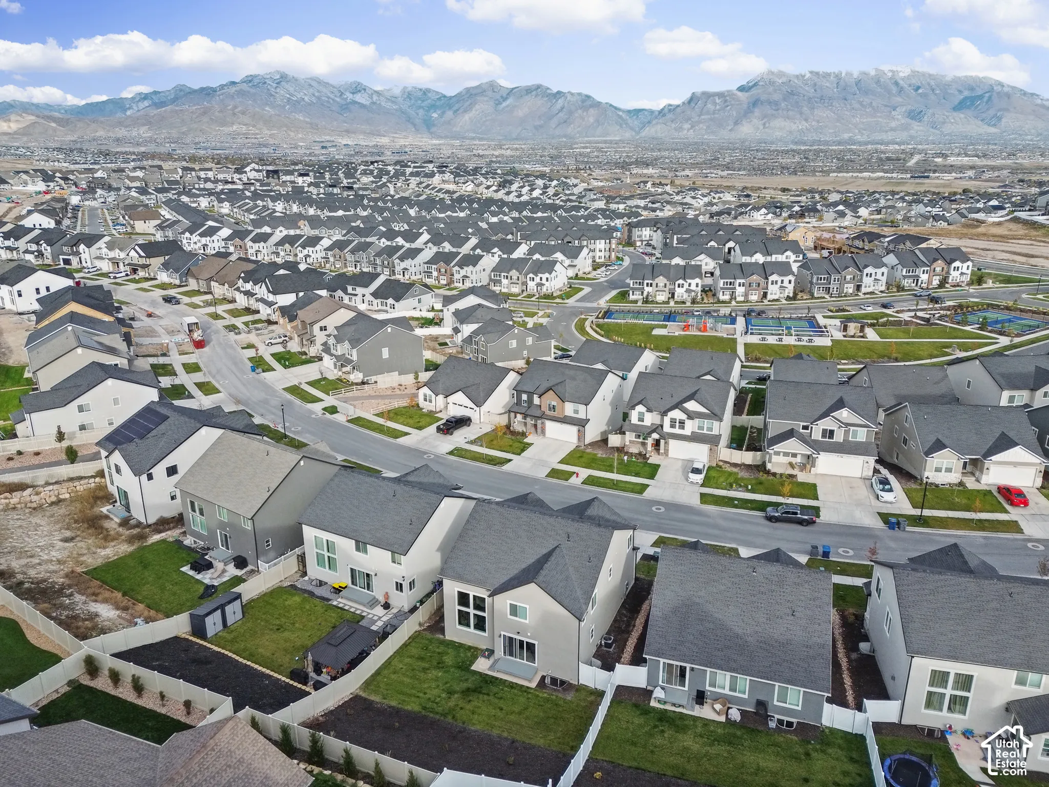 Aerial perspective of a residential neighborhood featuring mountain topography, multi-story single-family homes, and paved thoroughfares