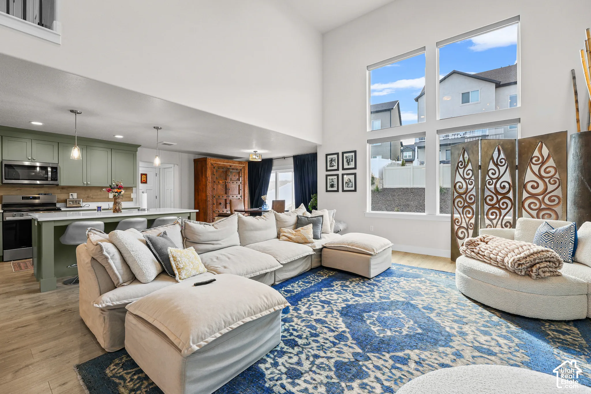 Open-concept space featuring double-height ceilings, expansive grid windows, wood-finish flooring, and a kitchen island with pendant lighting