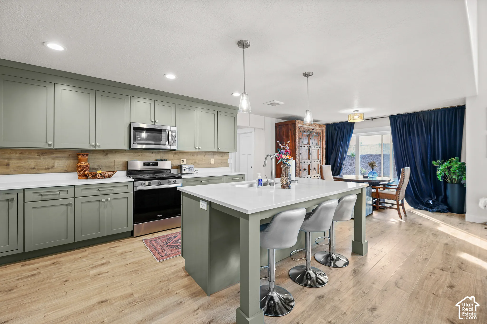 Kitchen featuring sage green cabinetry, white stone-finish countertops, wood-finish flooring, a central island with integrated sink, and recessed lighting
