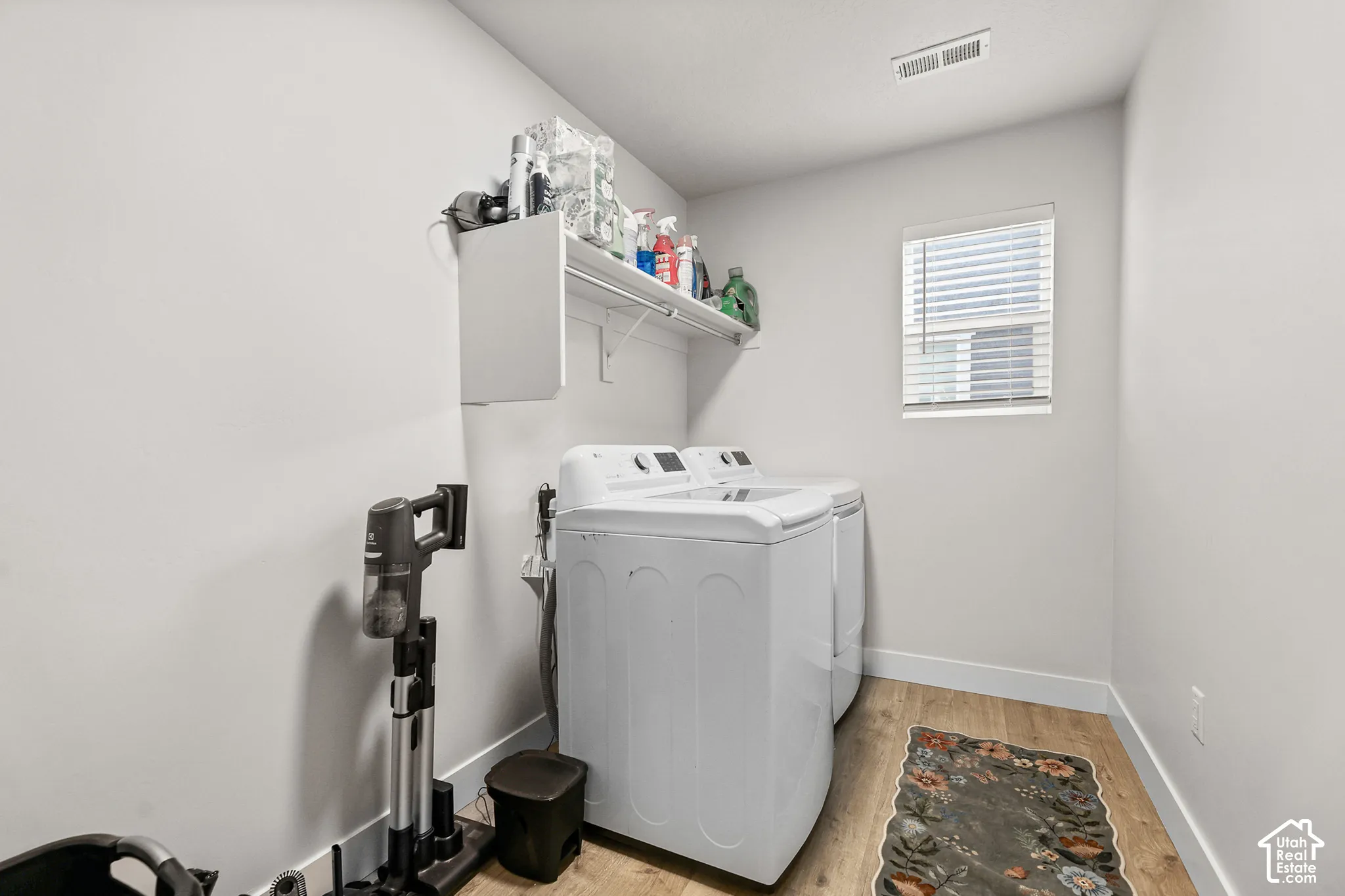 Utility area featuring wood-finish flooring, a wall-mounted white storage shelf, and a window with horizontal blinds
