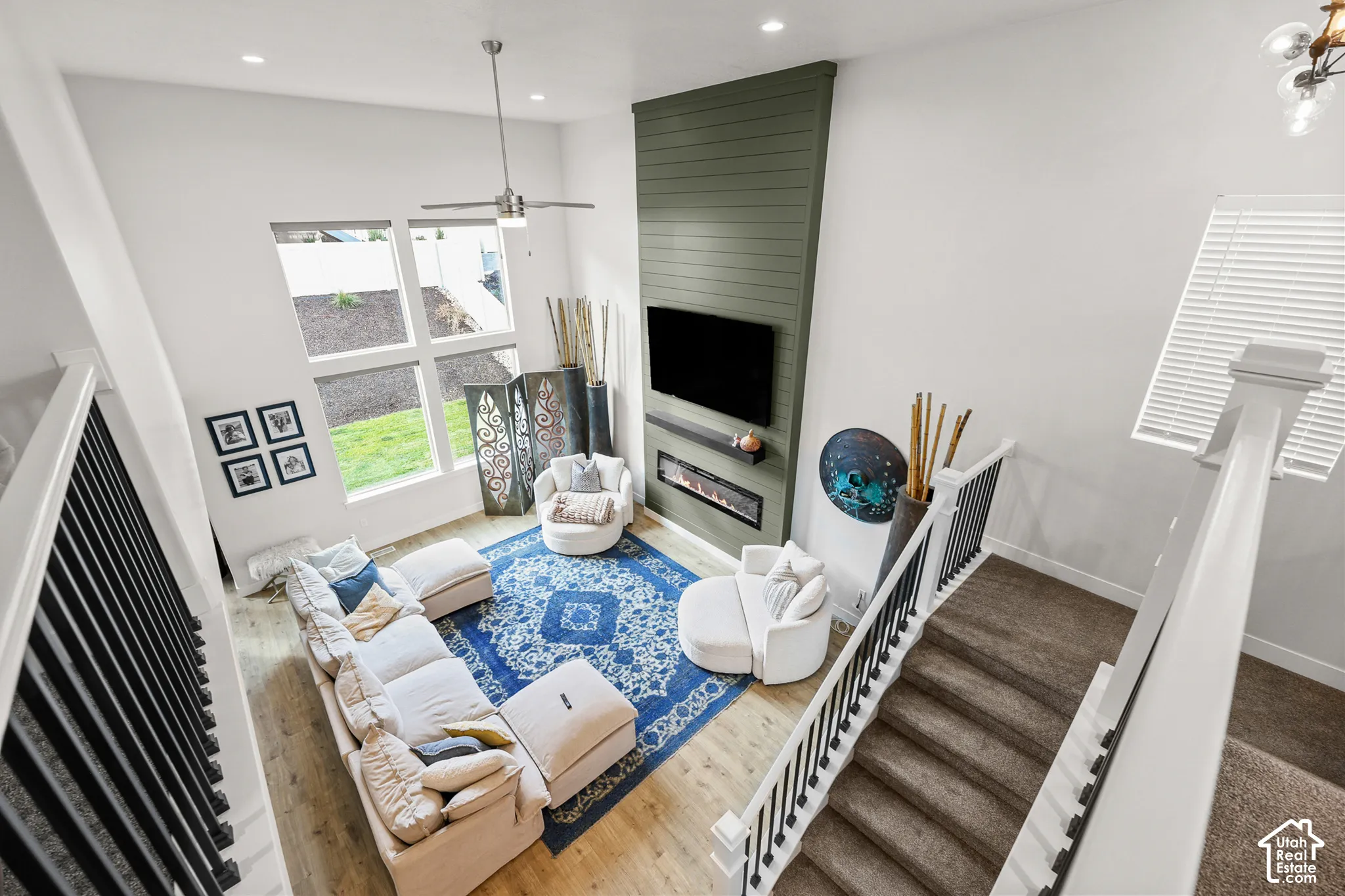 Two-story volume ceiling with floor-to-ceiling accent wall, vertical plank detailing, linear electric fireplace, recessed lighting, and wood-finish flooring