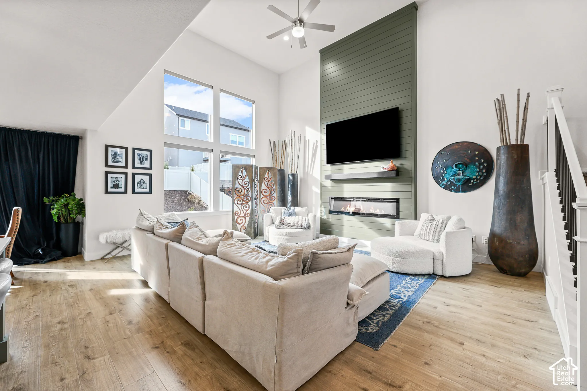 Living area featuring vaulted ceilings, wood-finish flooring, floor-to-ceiling accent wall with horizontal shiplap, inset linear fireplace, and oversized picture windows