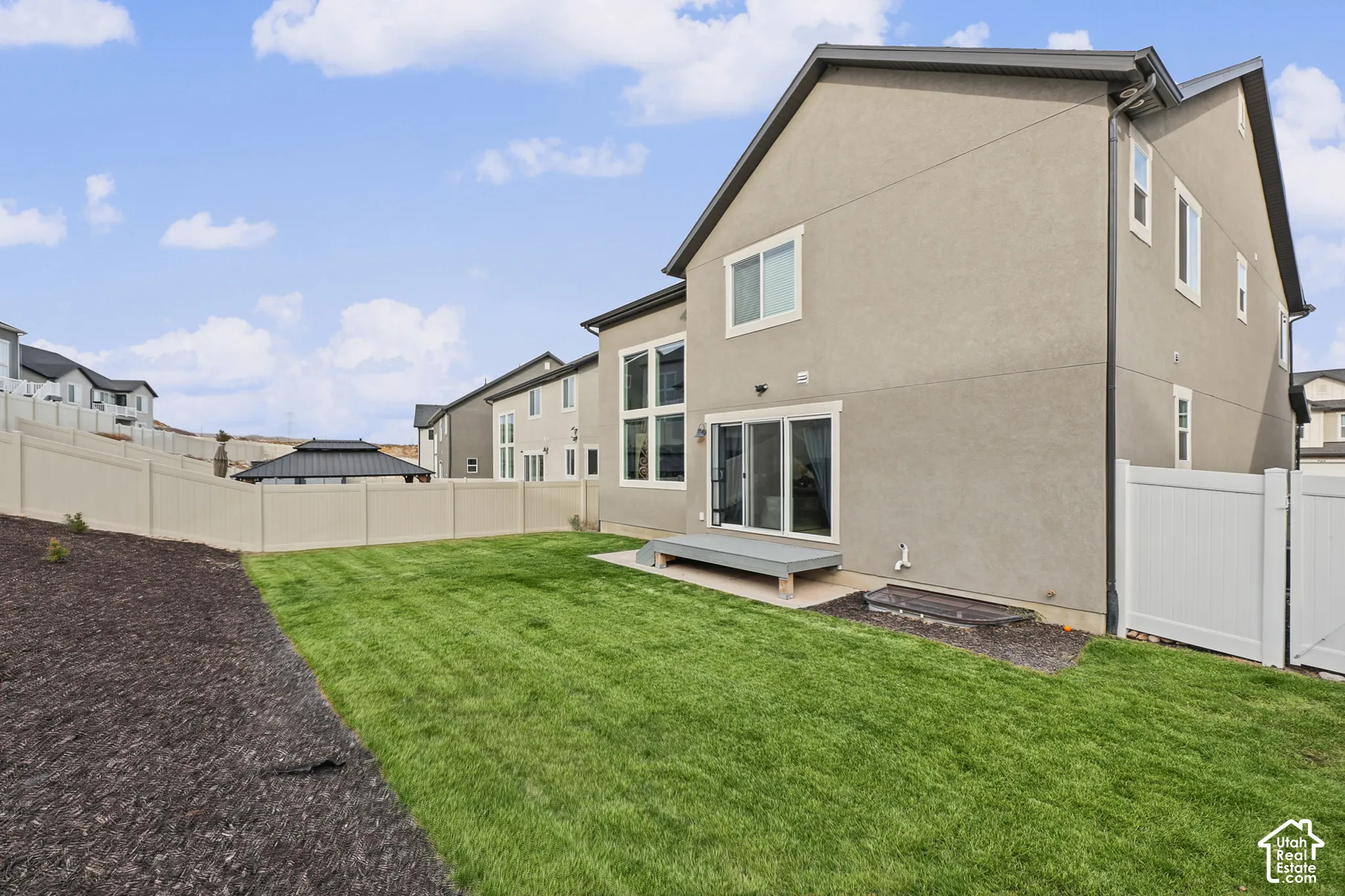 Rear exterior featuring stucco siding, multi-pane windows, sliding glass door, a low-profile platform deck, and full vinyl perimeter fencing enclosing a manicured lawn