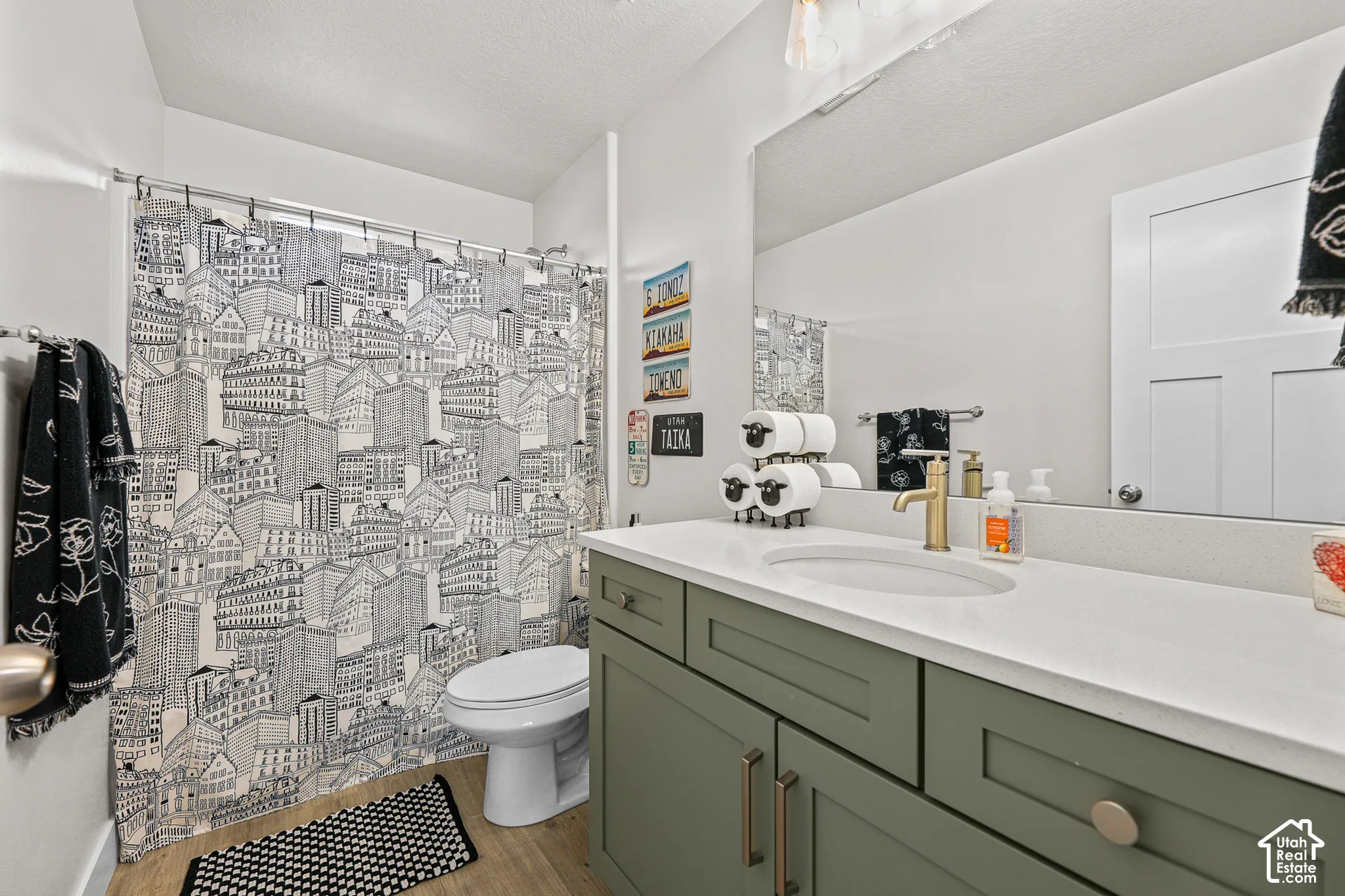 Bathroom featuring a green-toned shaker-style vanity, solid-surface countertop with an integrated oval sink, brass-finish faucet, and oversized wall-mounted mirror
