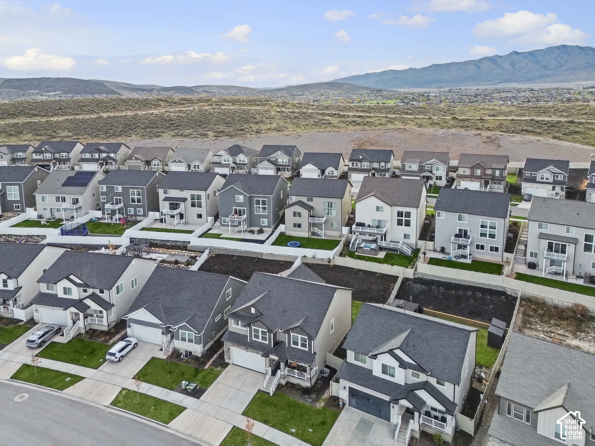 Aerial perspective featuring multi-story residential architecture, attached garages, paved driveways, fenced rear yards, and mountain backdrop