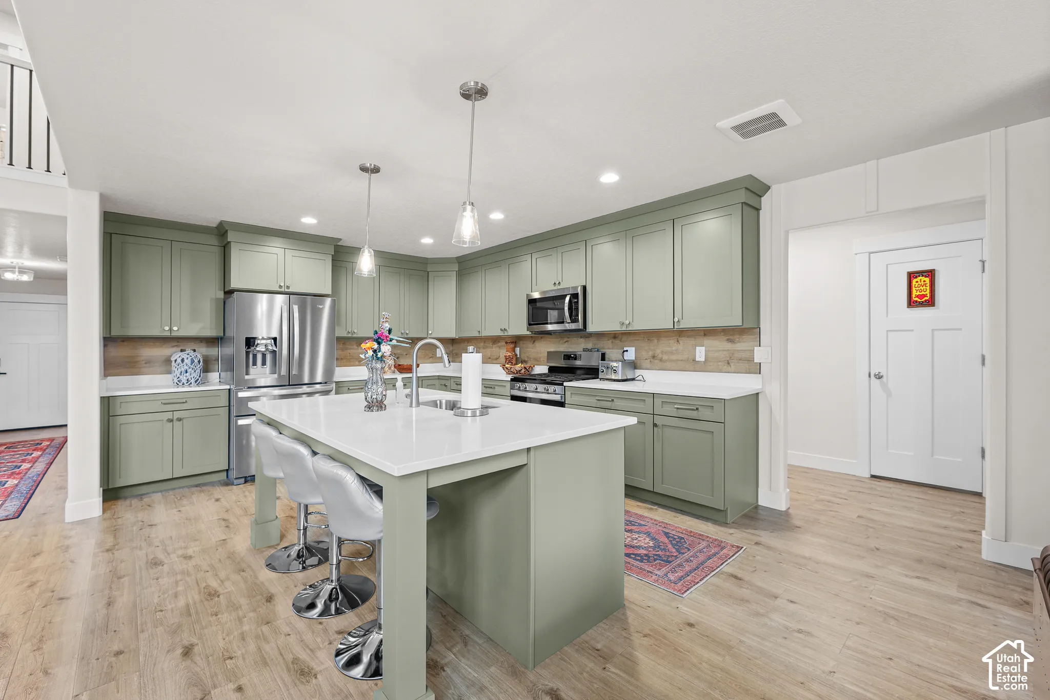 Kitchen featuring sage green cabinetry, a central island with a white countertop, wood-finish flooring, stainless steel appliances, and a wood-toned backsplash