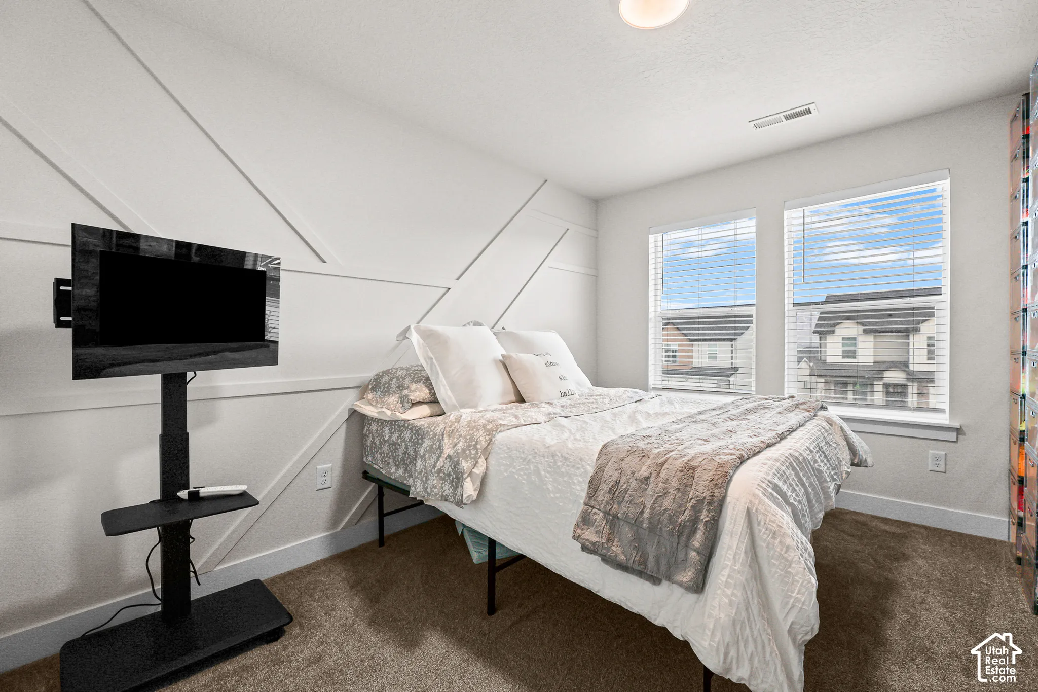 Bedroom featuring an accent wall with geometric millwork, neutral carpeting, and dual windows with horizontal blinds