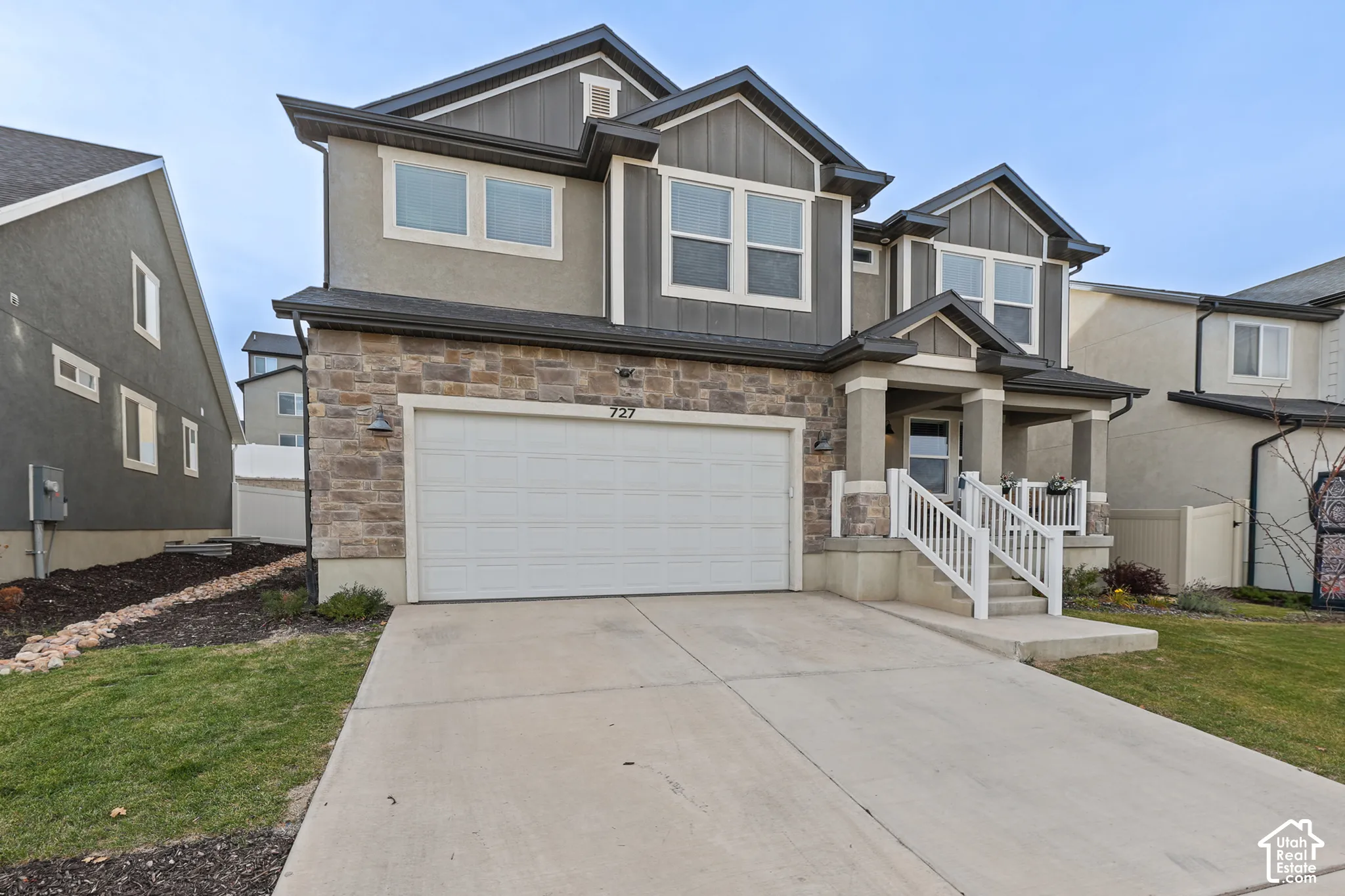 Two-story exterior featuring a stone facade, mixed-material siding, a double-car garage, and a covered entryway with a staircase and white railing